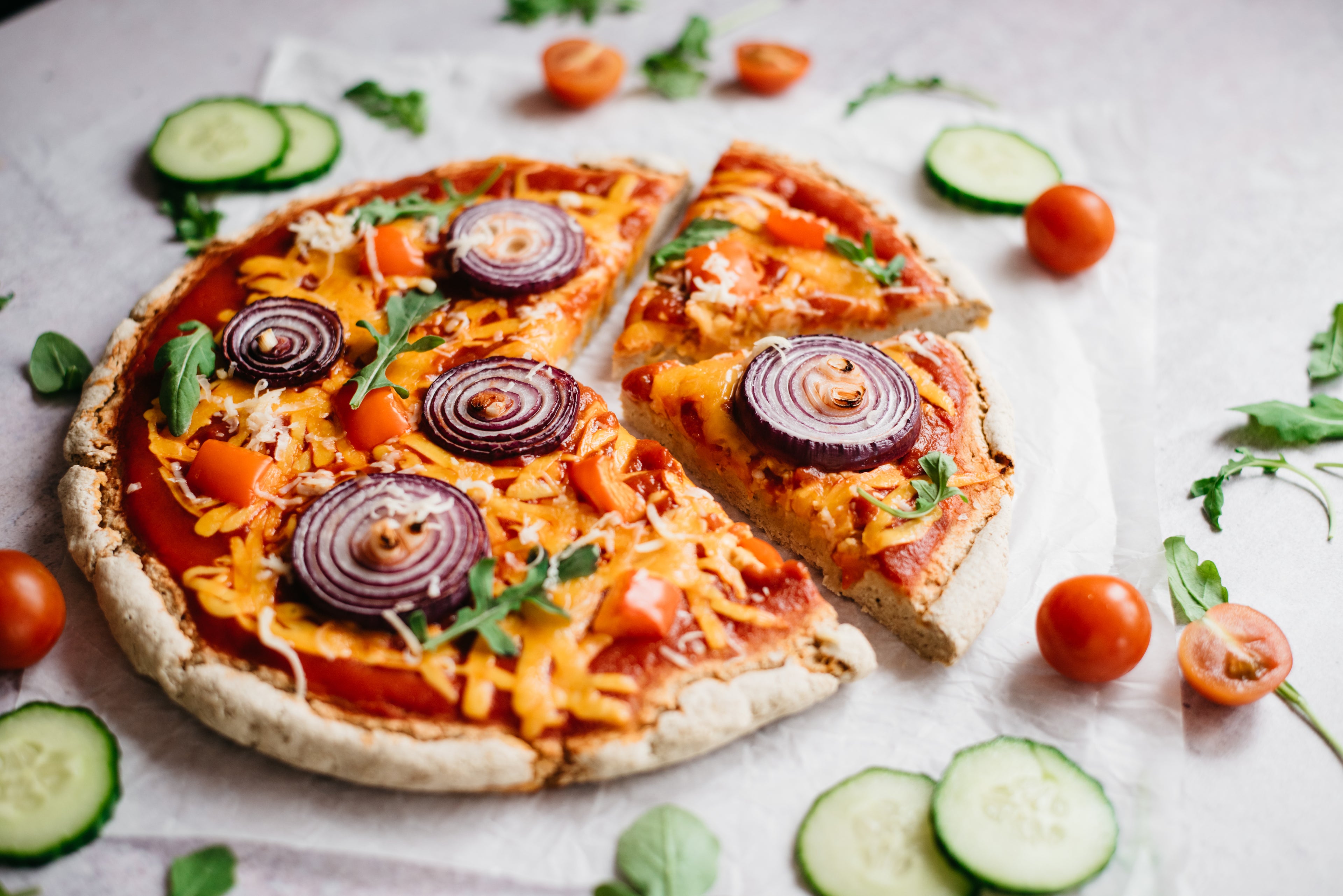 Pizza on baking paper with slice cut out and salad