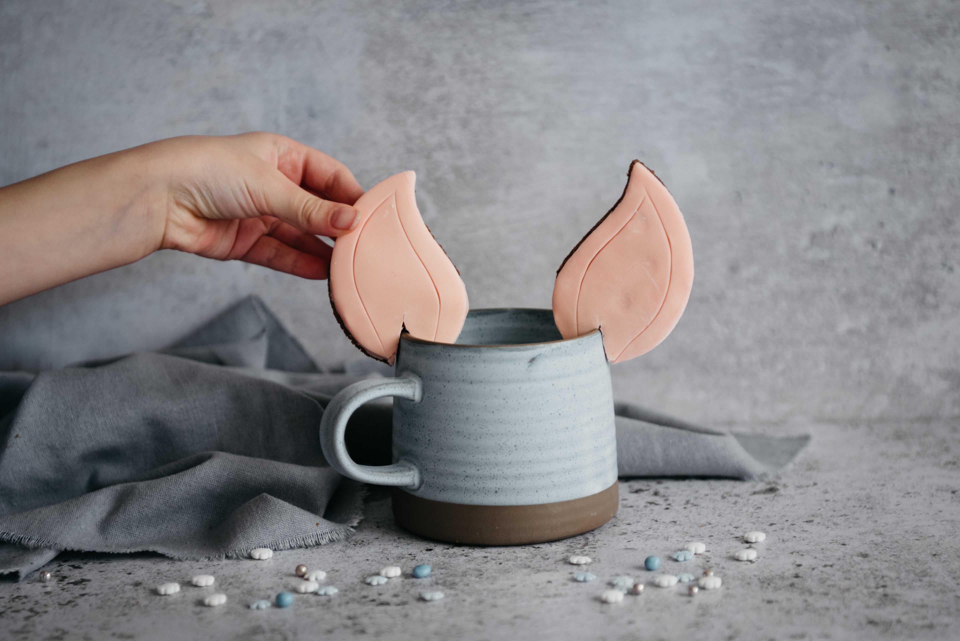 Hand reaching to the Elf Ears Gingerbread Cookies on the edge of a blue mug with a hot drink