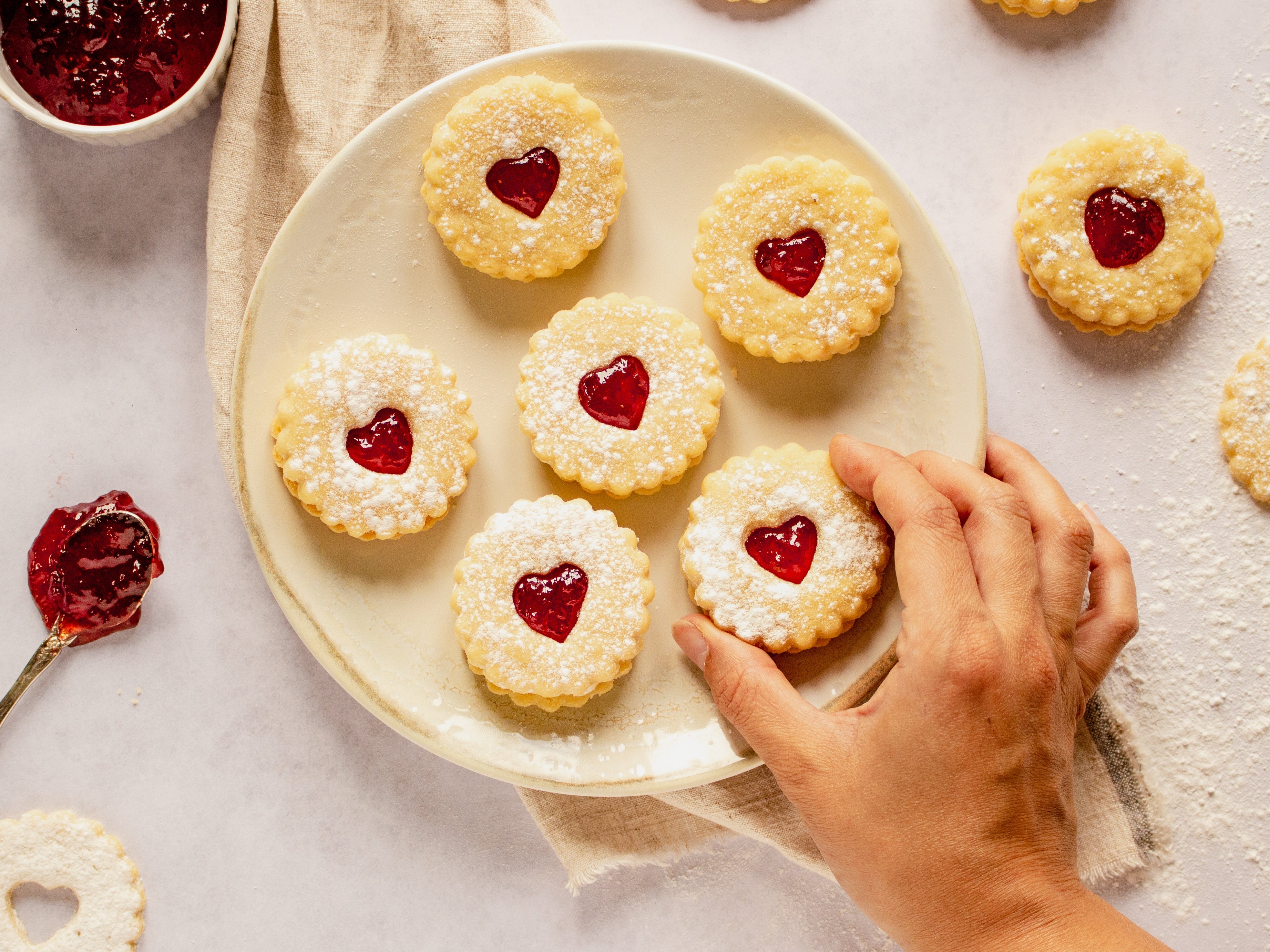 Six homemade jammy dodgers on a white plate with a hand reaching for them
