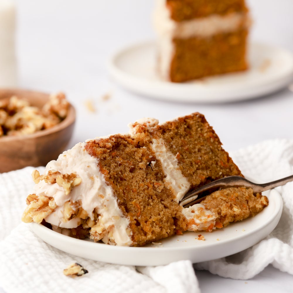 A chunky slice of carrot cake with buttercream on top and in the middle, a fork is tucking into the slice.