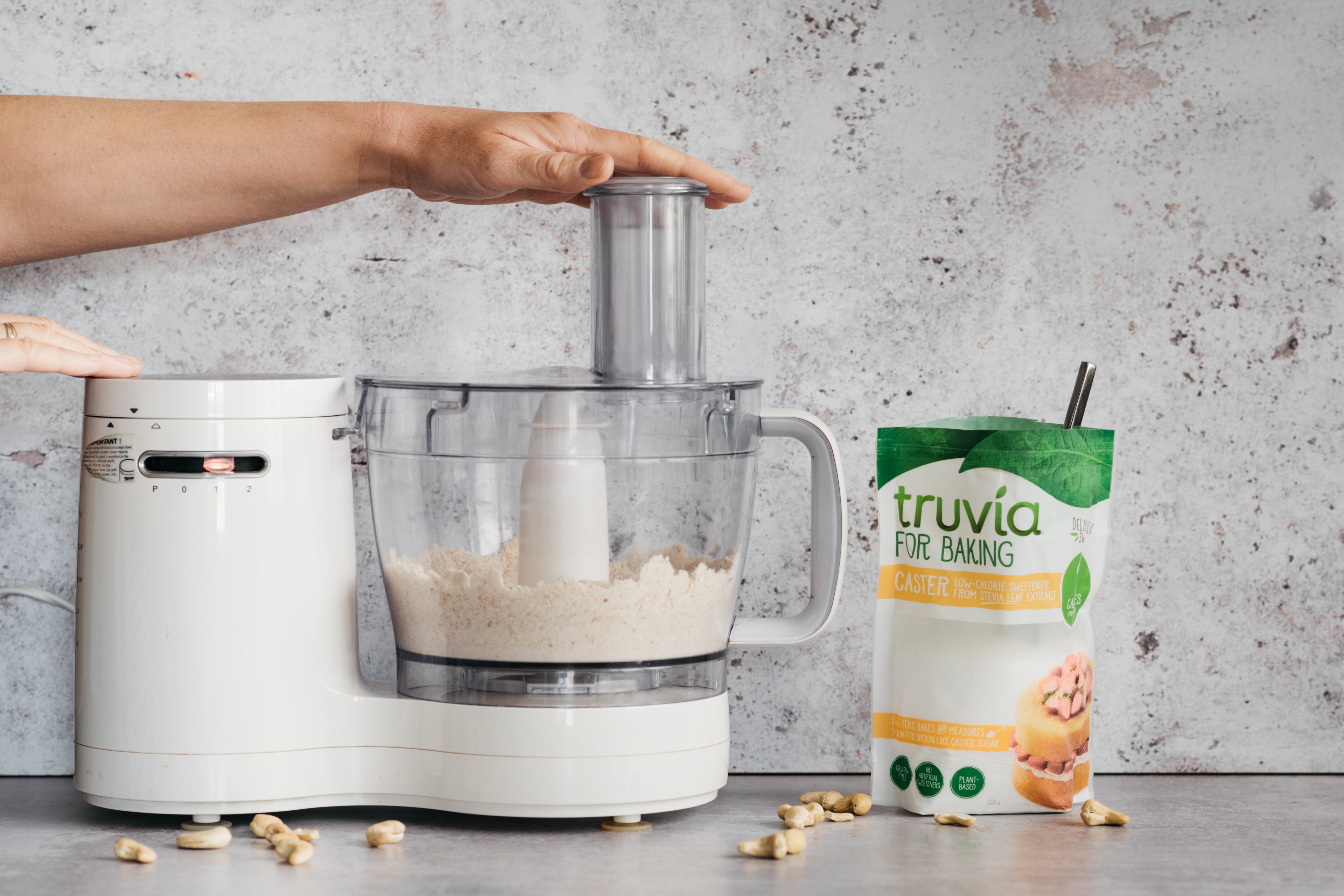 Hand using food processor to blend the mix for No-Bake Millionaire Bites next to a bag of Truvia for Baking Caster