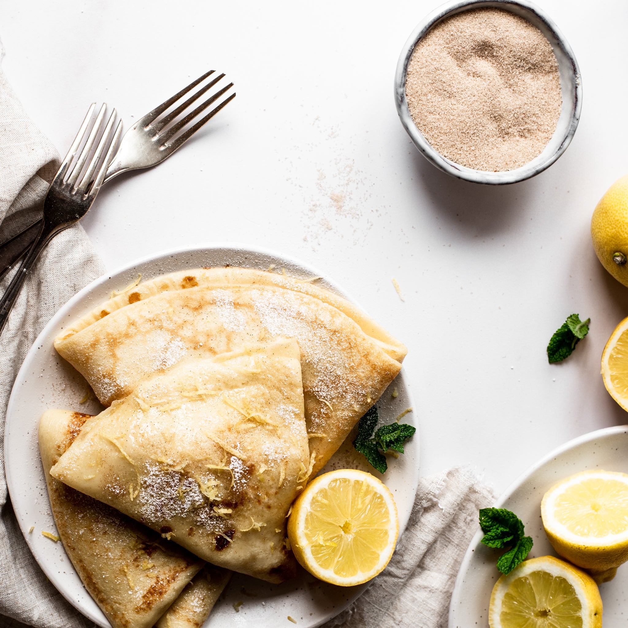 Fresh pancakes folded on a plate with zested lemon and sugar topping