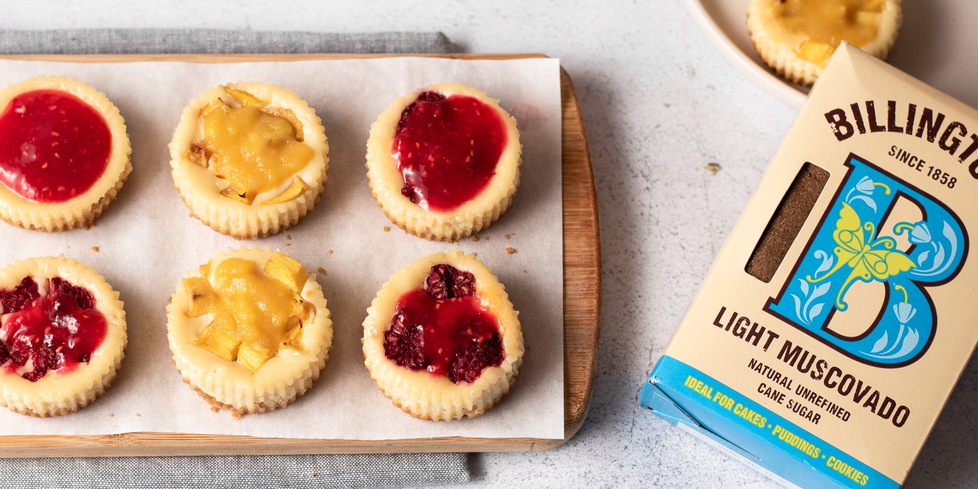 Mini cheesecakes topped with fruit on a wooden board next to sugar pack