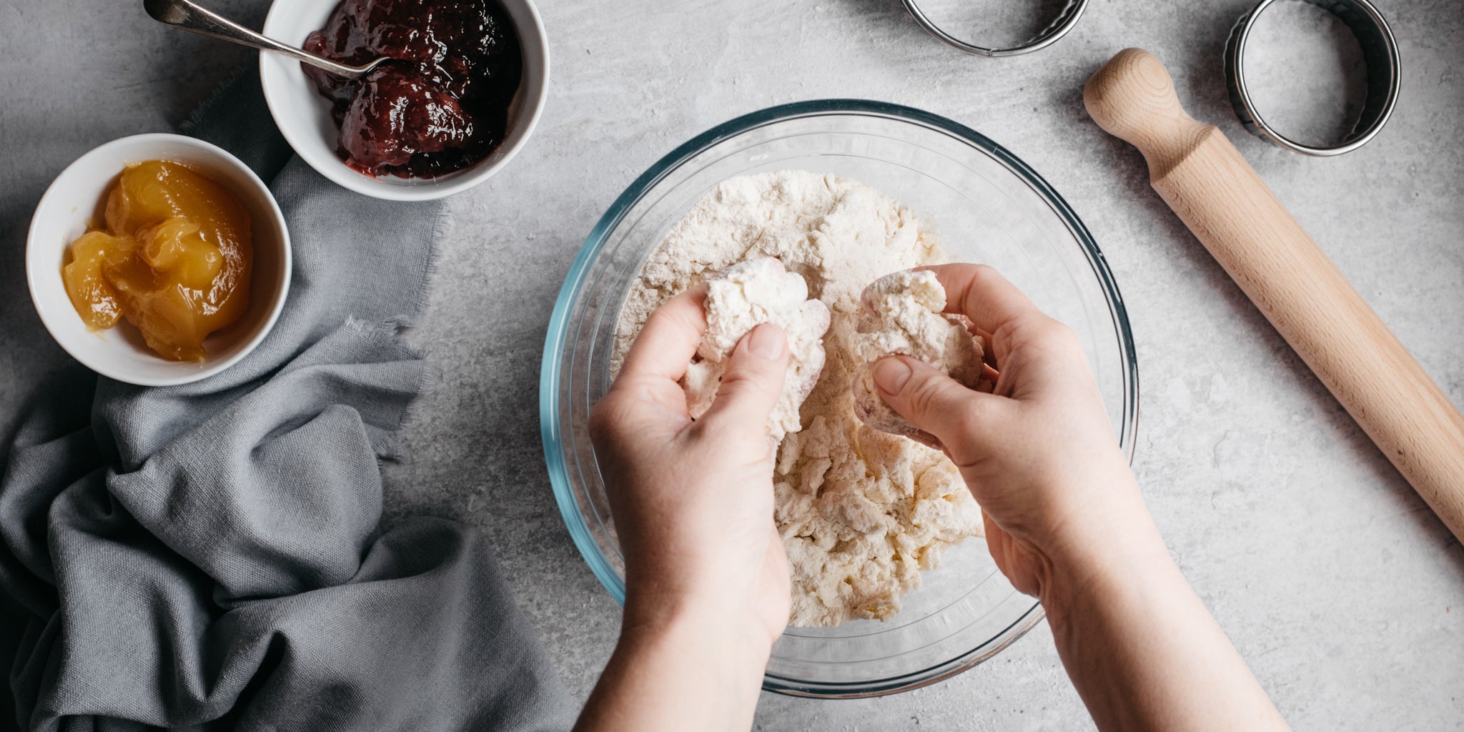 Hands combining the mixture for Strawberry Jam Tarts next to a bowl of strawberry and apricot jam