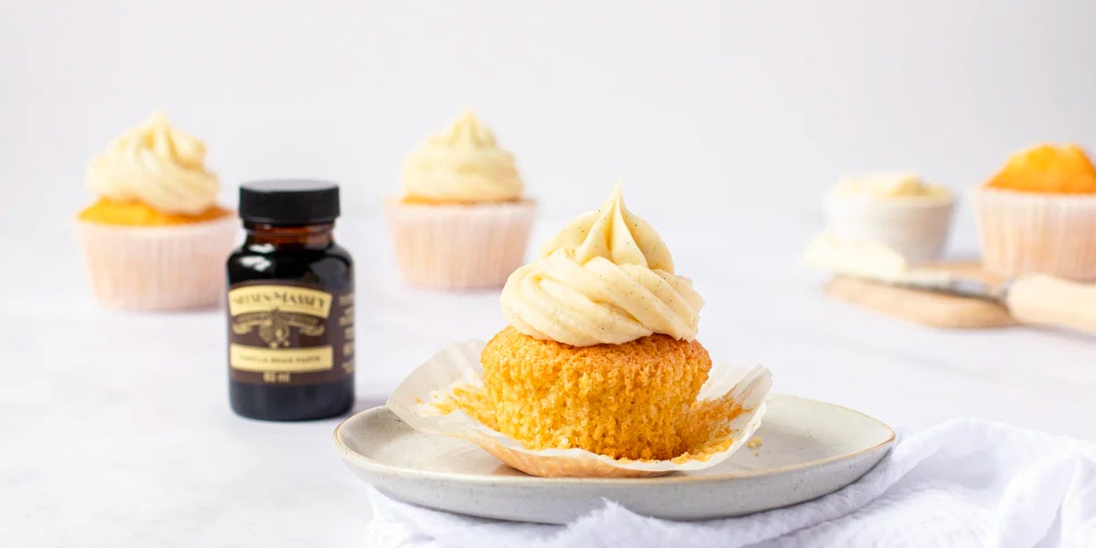 Vanilla cupcake with buttercream icing next to a bottle of Nielsen-Massey Vanilla Bean Paste
