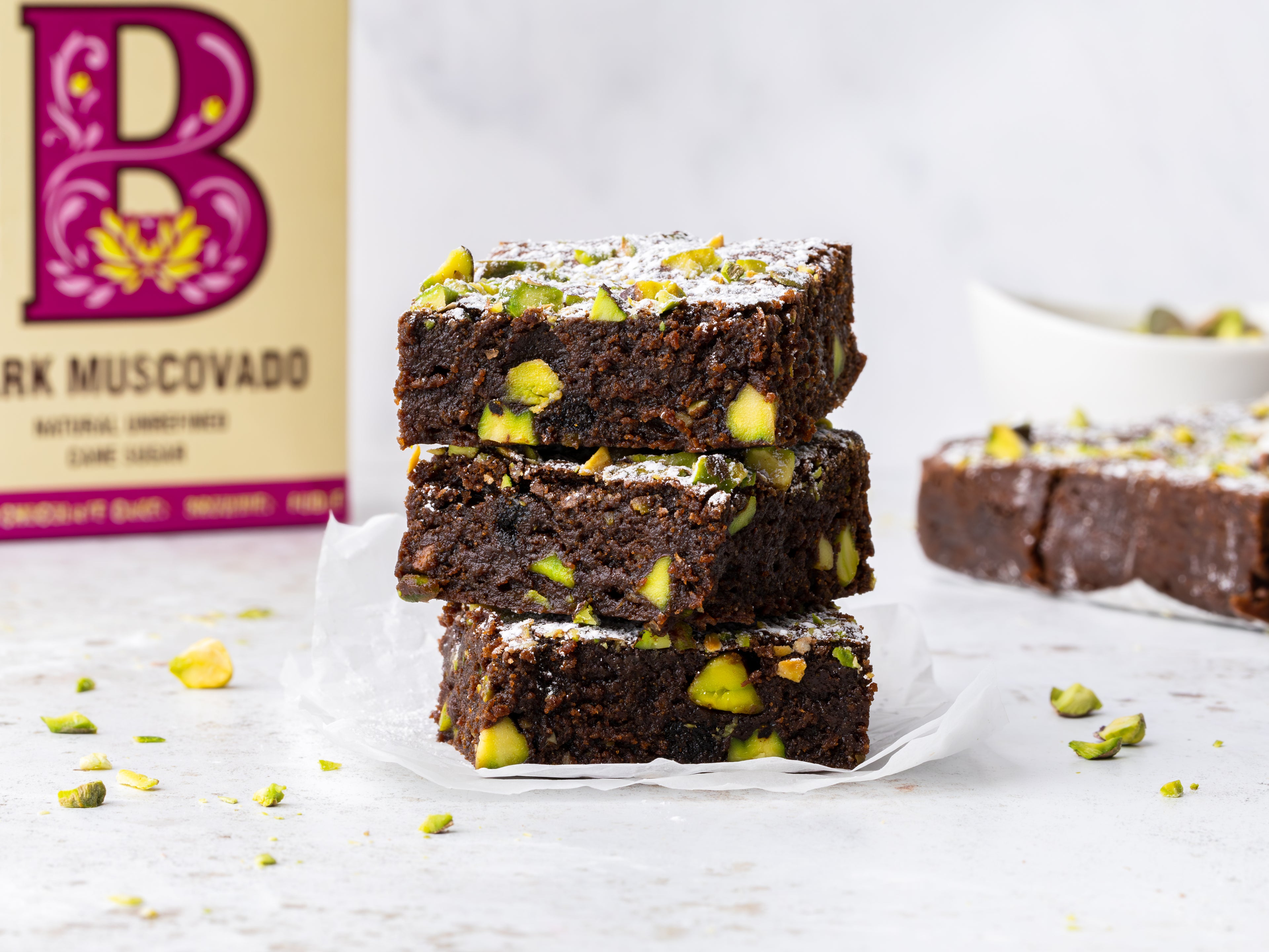 Pistachio Brownies stacked on top of each other infront of sugar pack