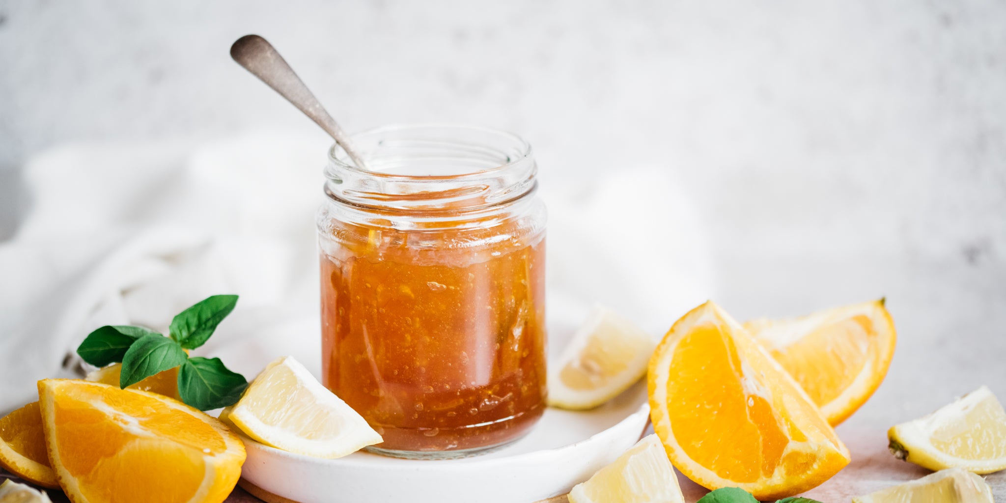 Open jar of marmalade with spoon inserted and sliced oranges beside it