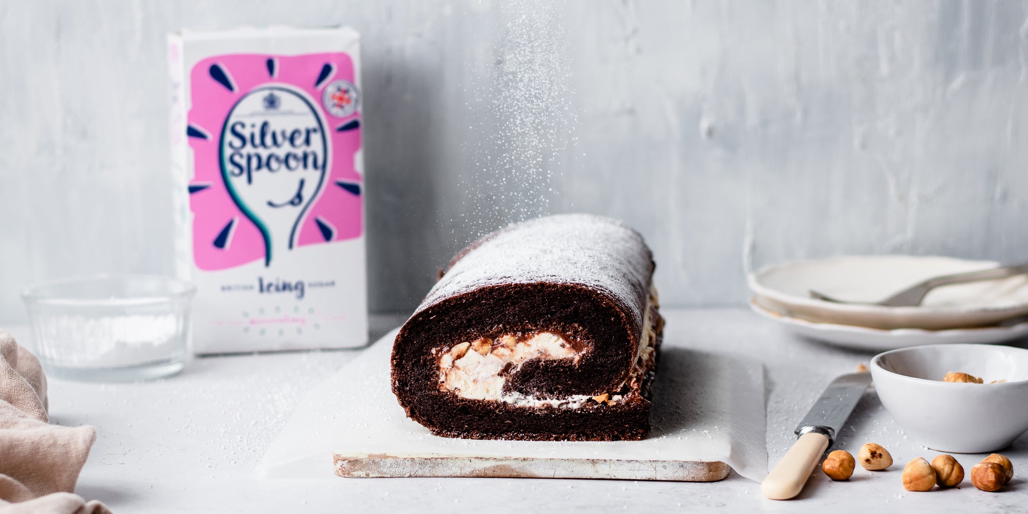 Chocolate Roulade on parchment paper on a serving board, with a box of Silver Spoon Icing Sugar in the background