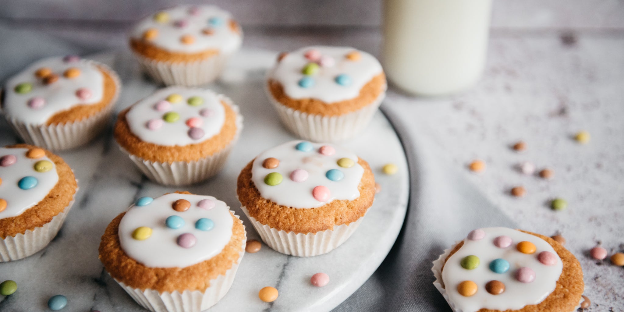 Close up view of Wholemeal Fairy Cakes on a marble cake stand, decorated with icing and smarties