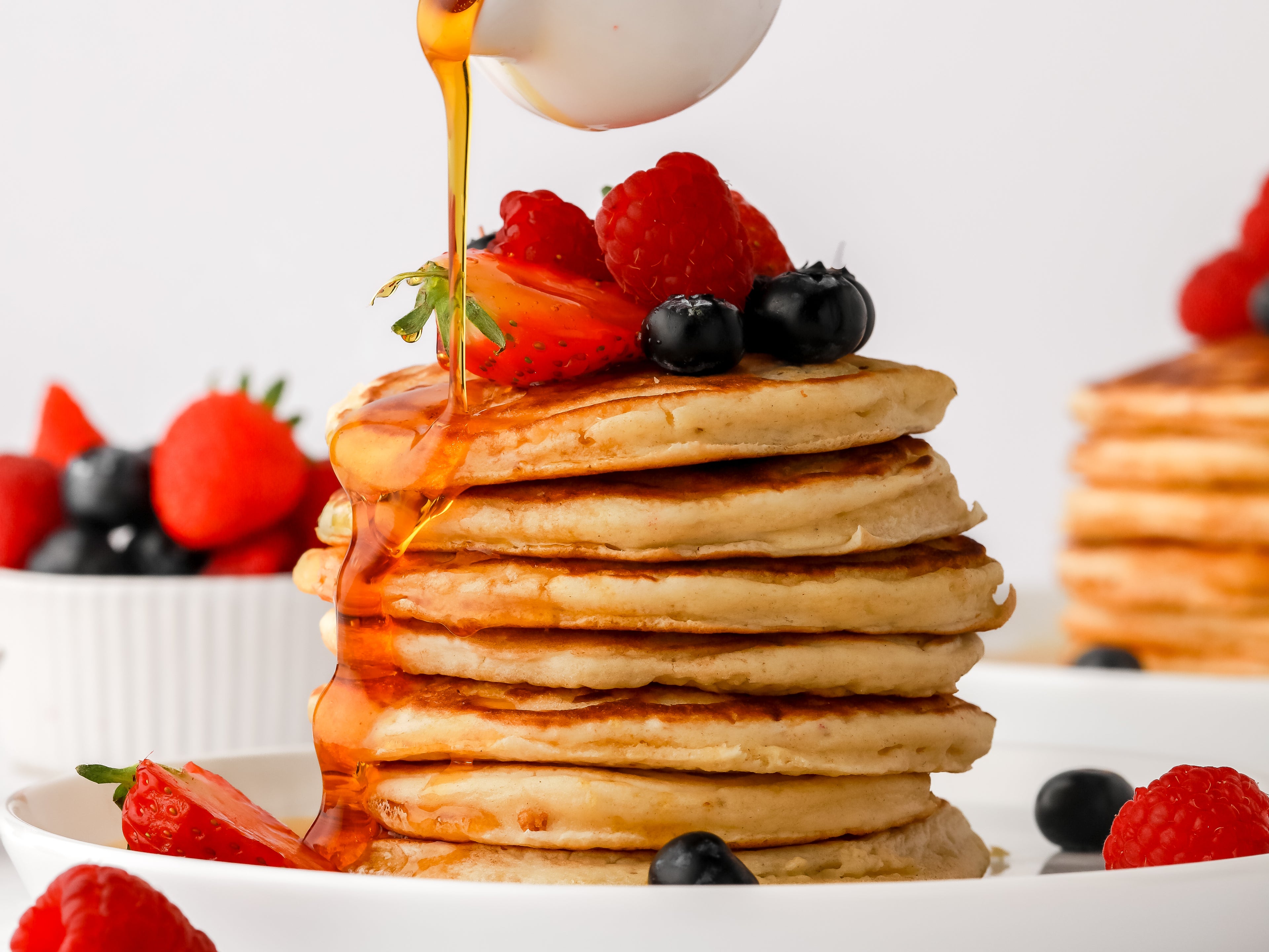 Stack of American Pancakes with fruit on top and sauce drizzling down the sides