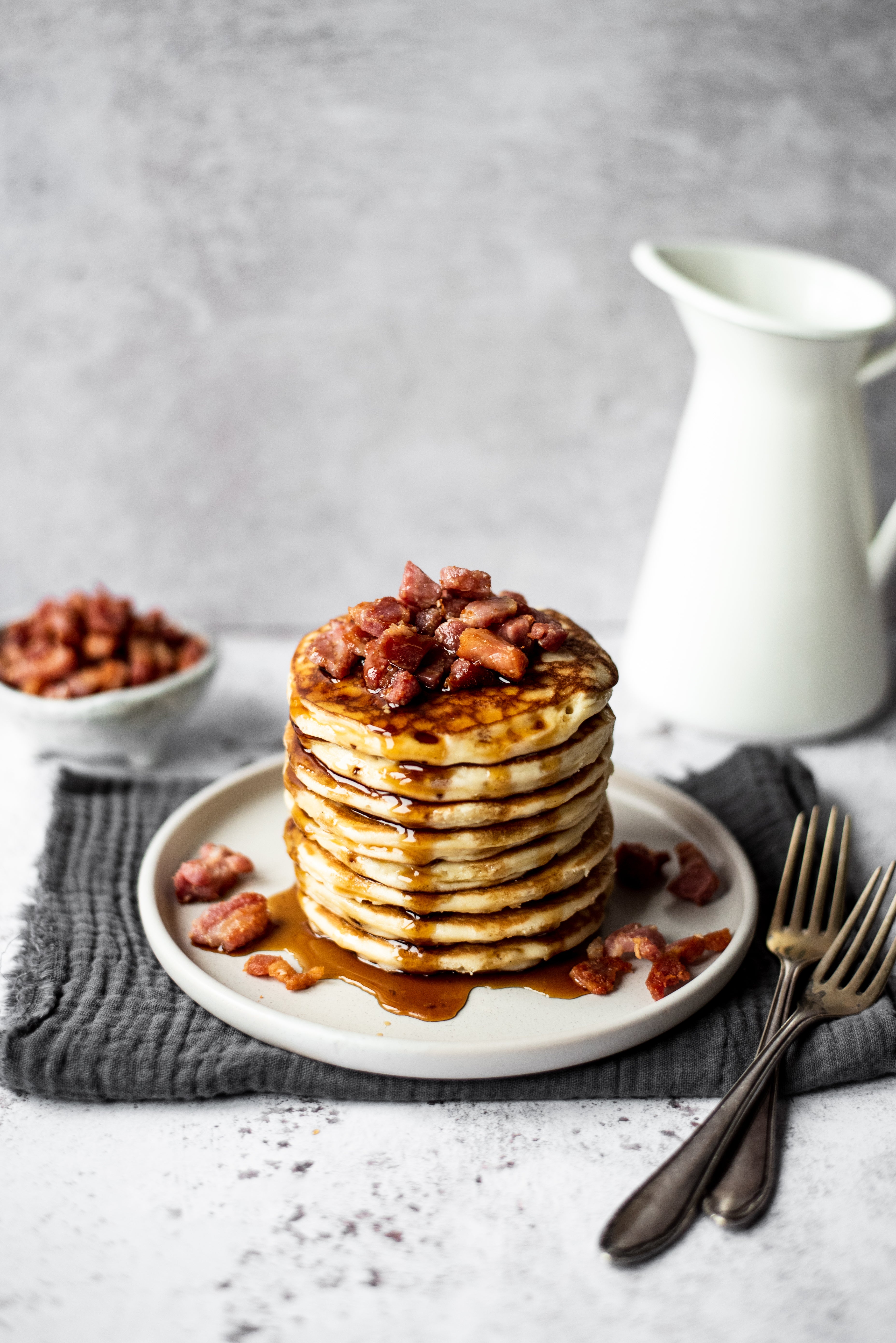 Stack of pancakes topped with bacon and maple syrup