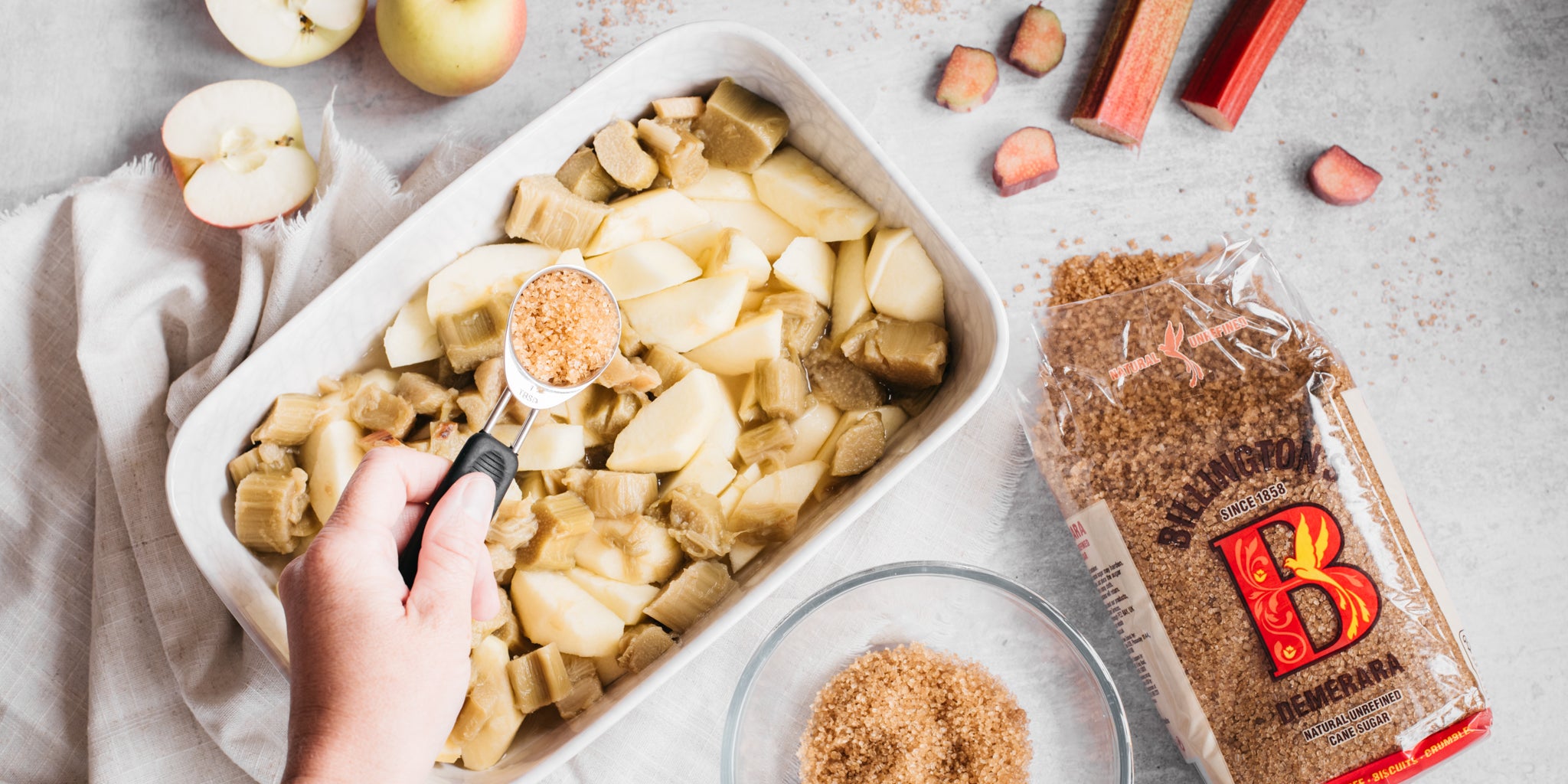 Hand sprinkling sugar on top of apple in a baking dish