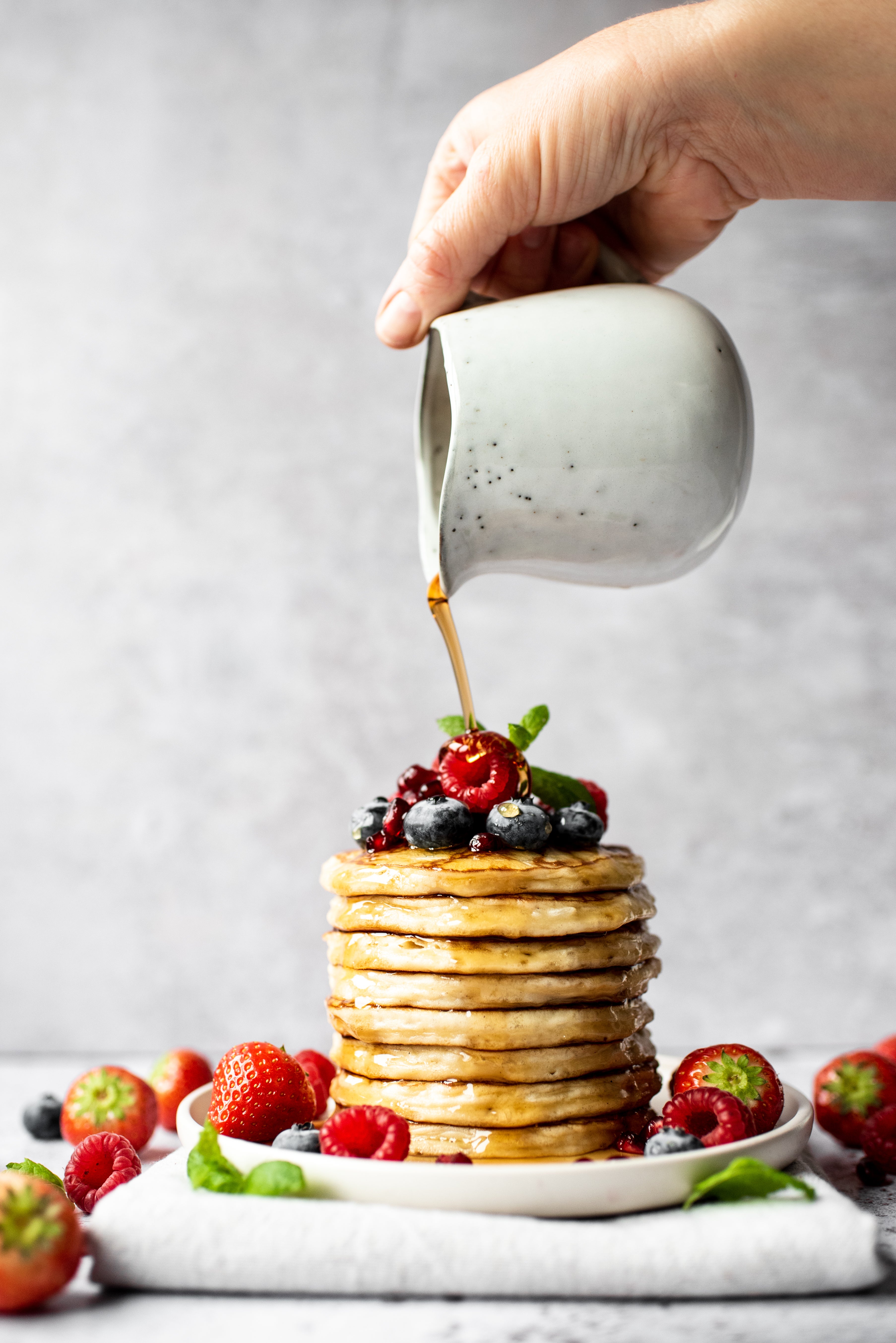 Pouring maple syrup over a stack of American pancakes