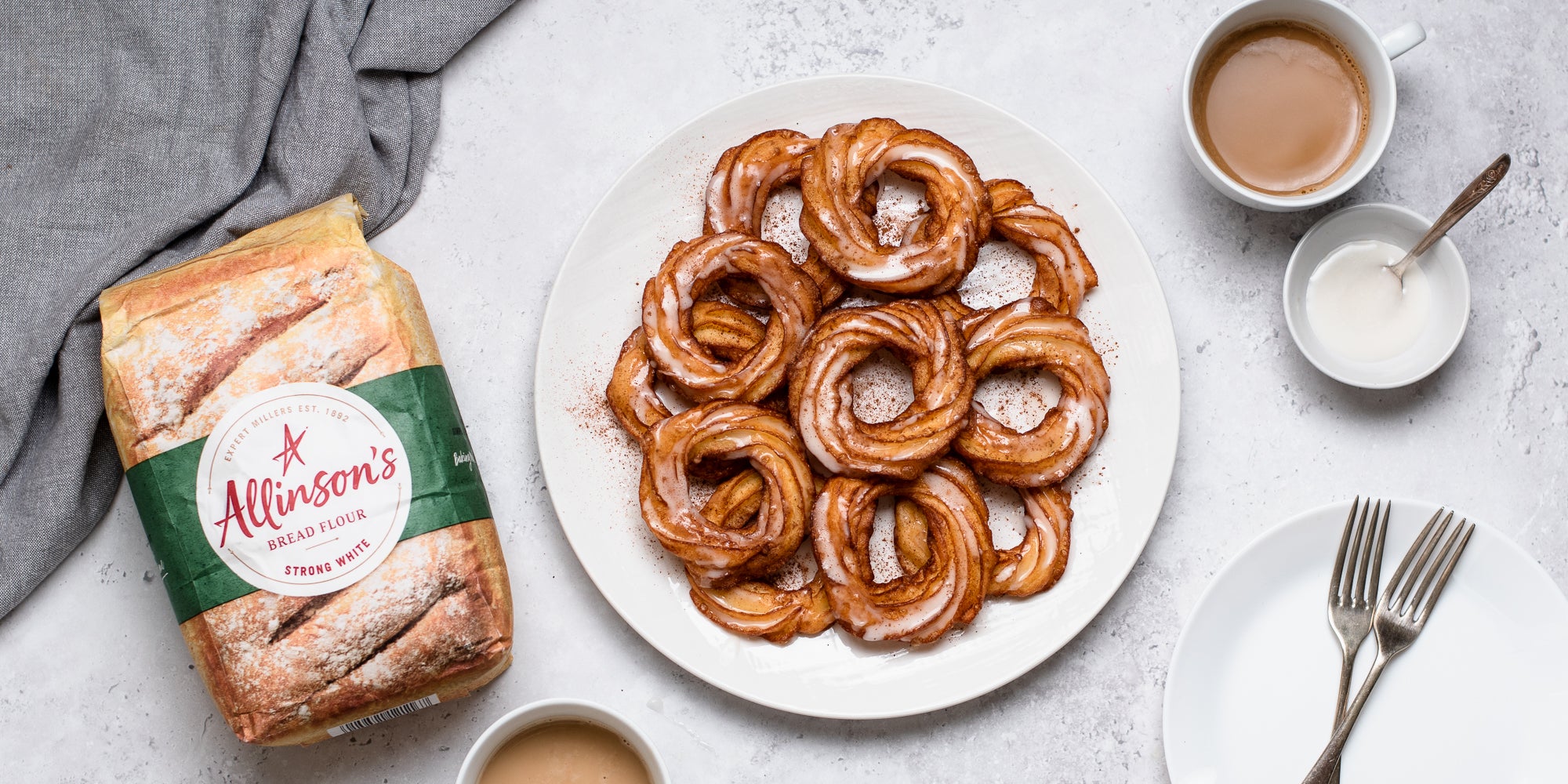 Apple Cider Crullers on a plate, next to a bag of Allinson's Strong White Flour, topped with icing.