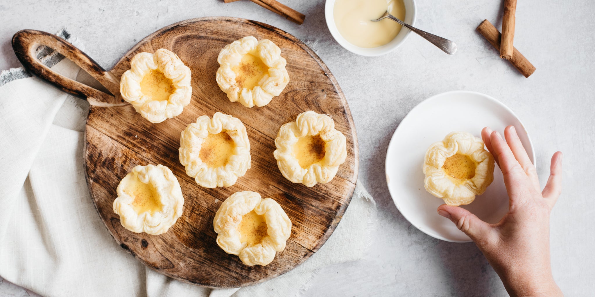 Portuguese Custard Tarts on a circular wooden board with a hand reaching in 