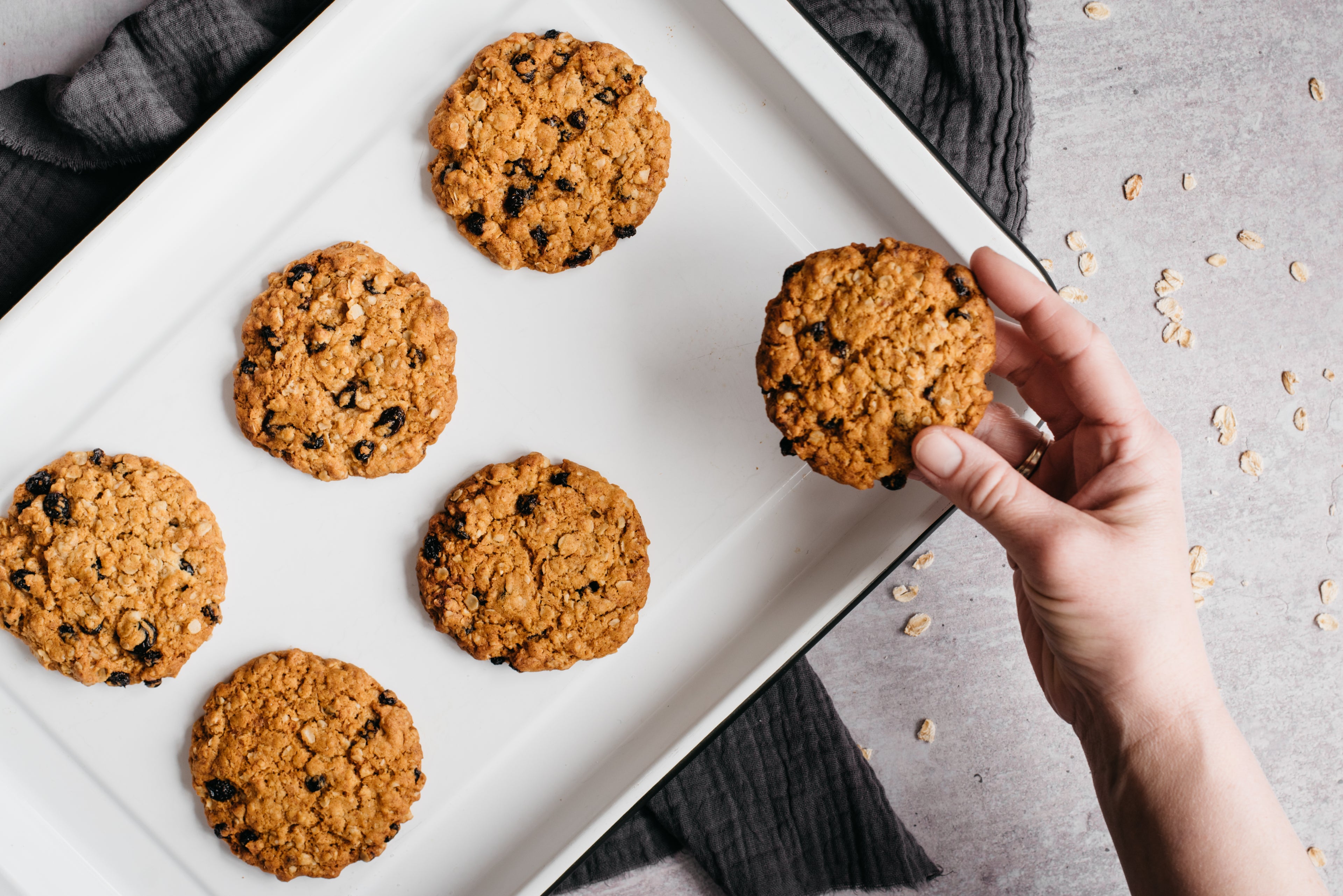 Hand reaching for a Oat & Raisin Cookies freshly baked on a baking tray