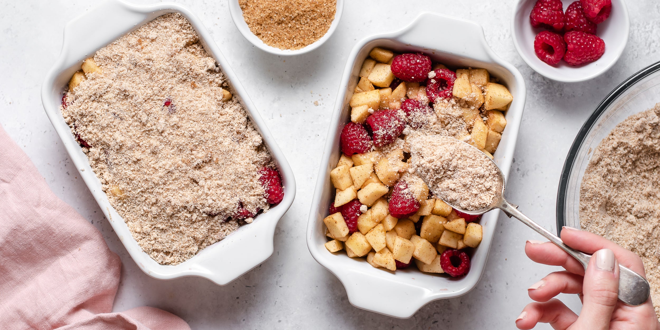 Chopped fresh apple and raspberries being sprinkled with a crumble topping ready to bake Apple & Raspberry Crumbles