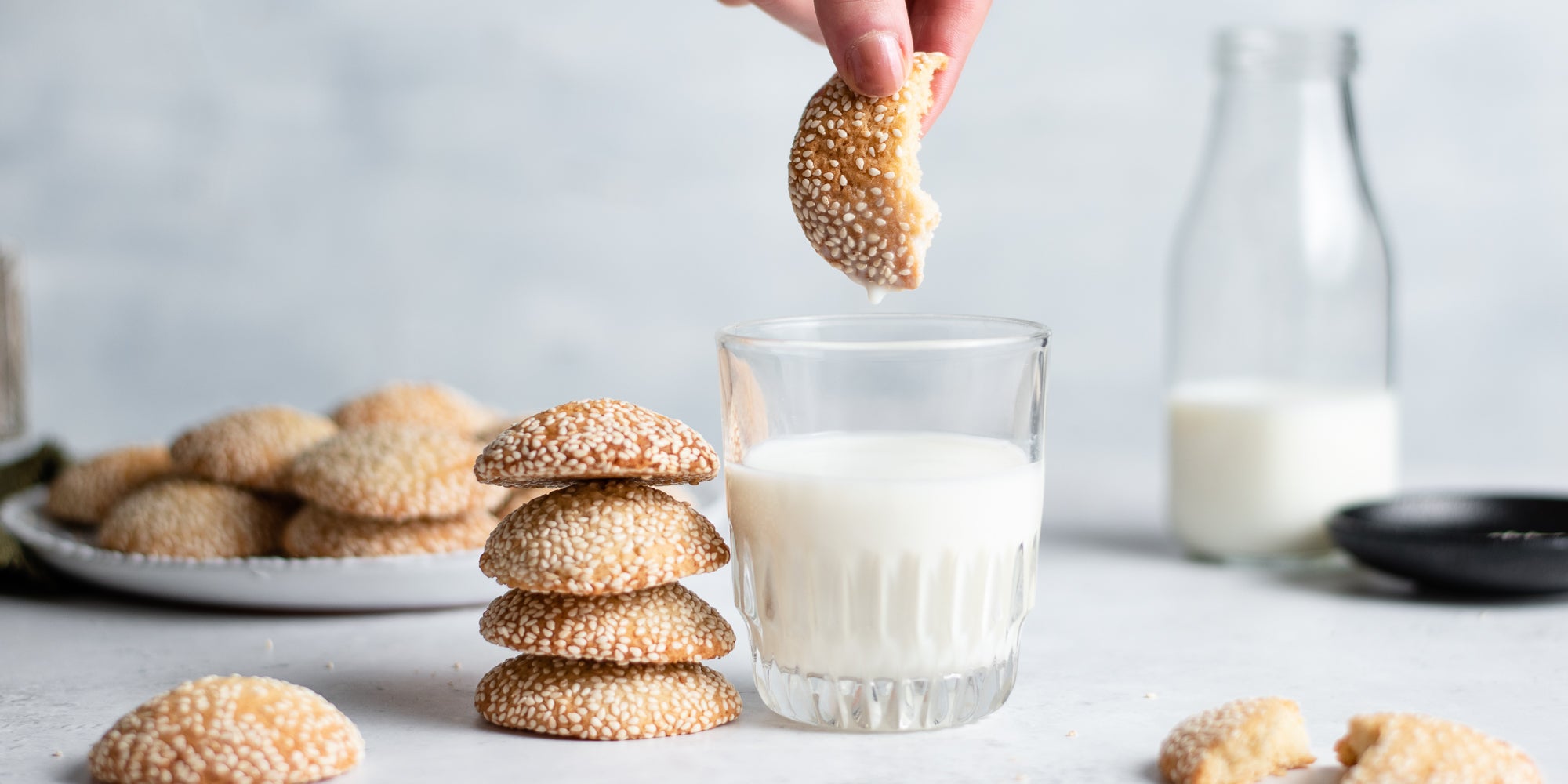 A hand dipping a sesame cookie into a glass of milk