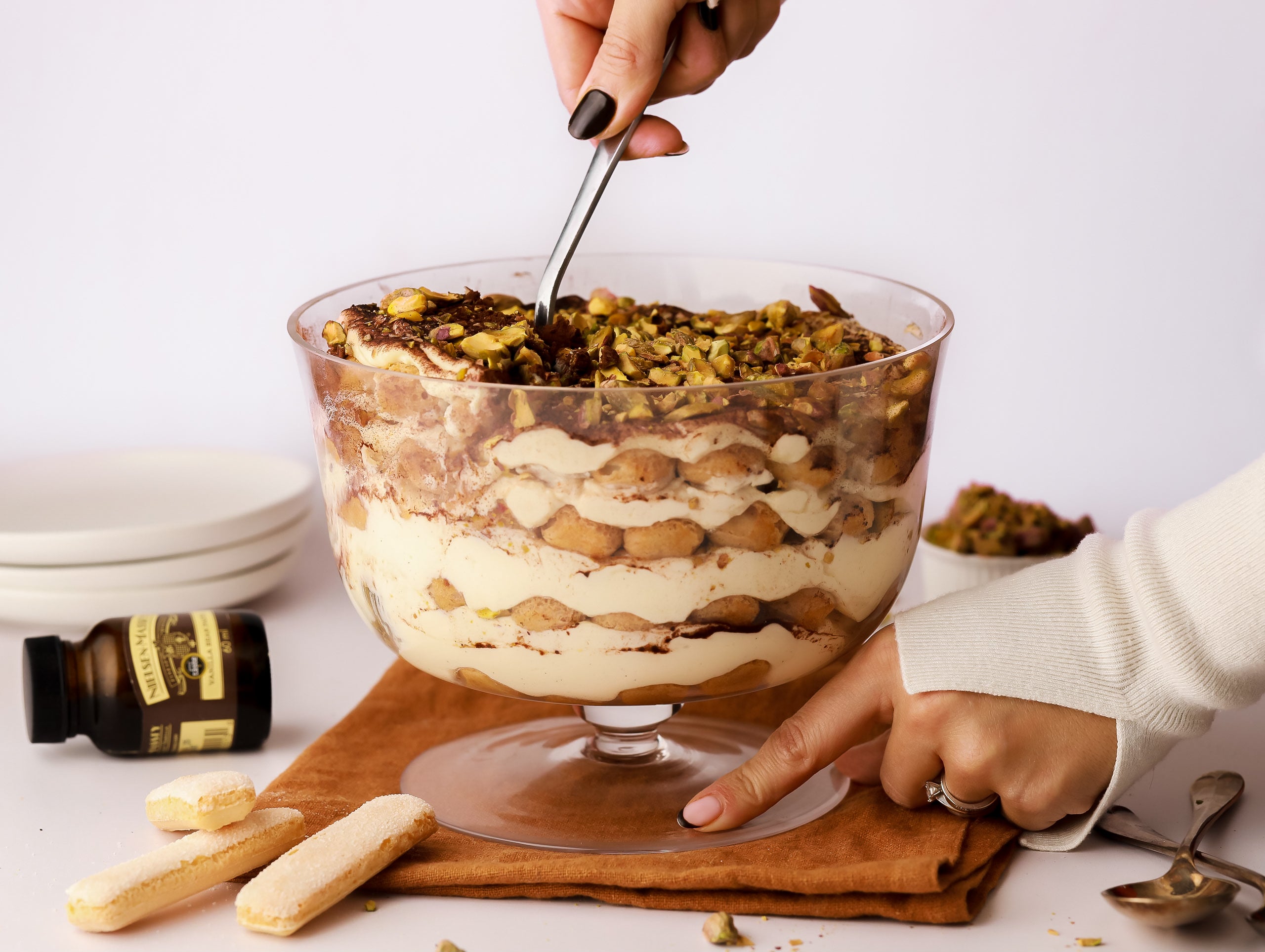 Hand spooning out a portion of tiramisu from a large glass bowl