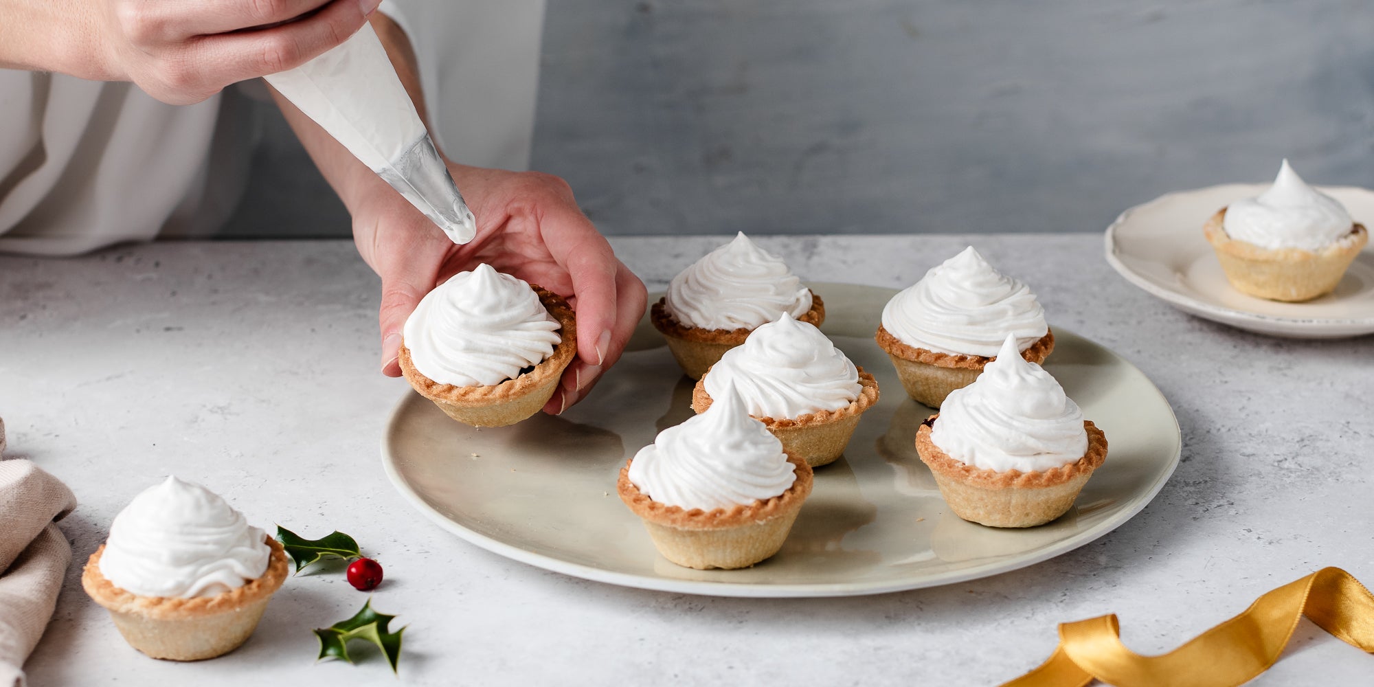 Meringue Topped Mince Pies with a hand holding a pie, piping it with meringue 