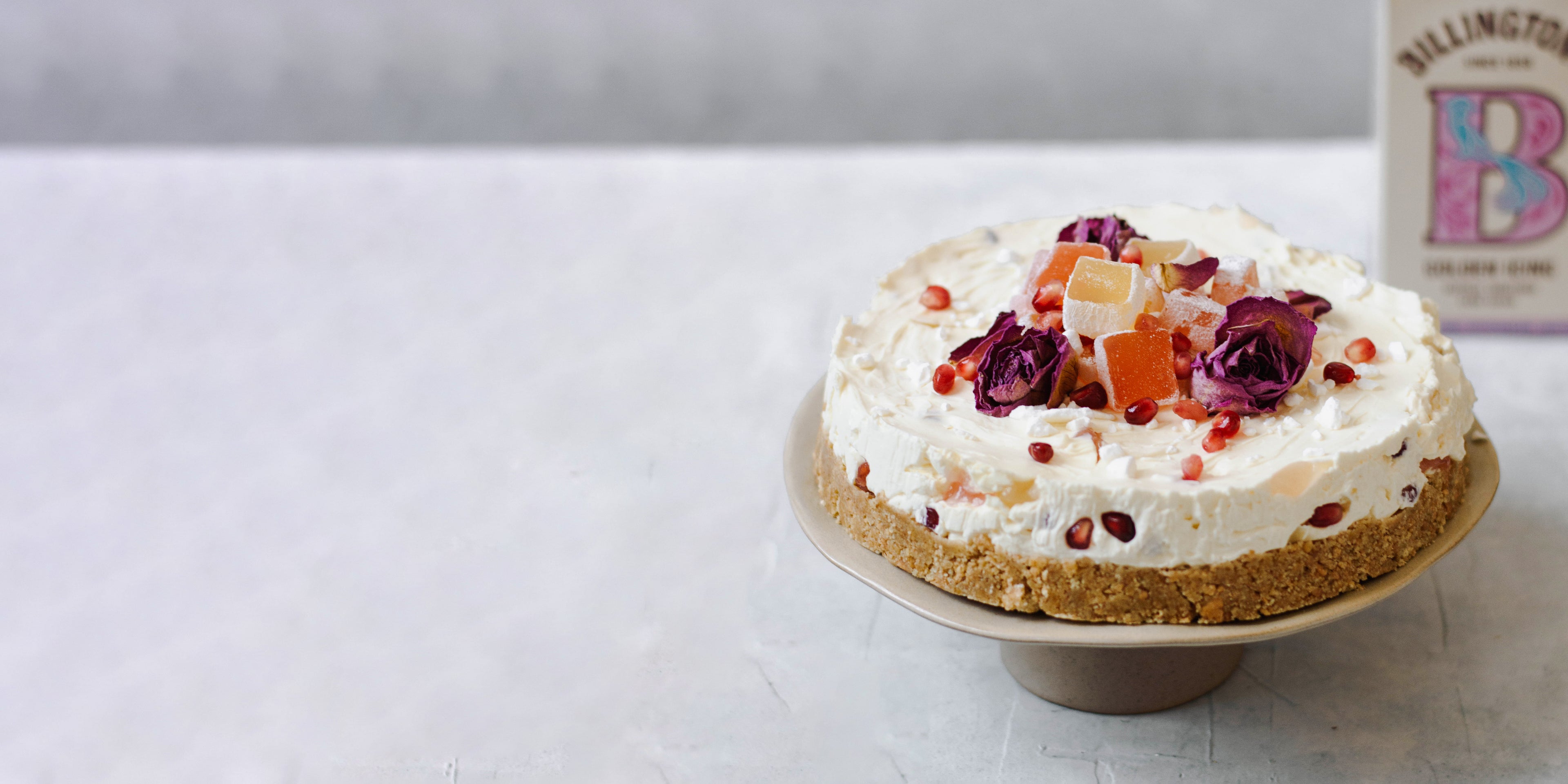 Turkish delight cheesecake on a cake stand, with a box of Billington's golden icing sugar in the background