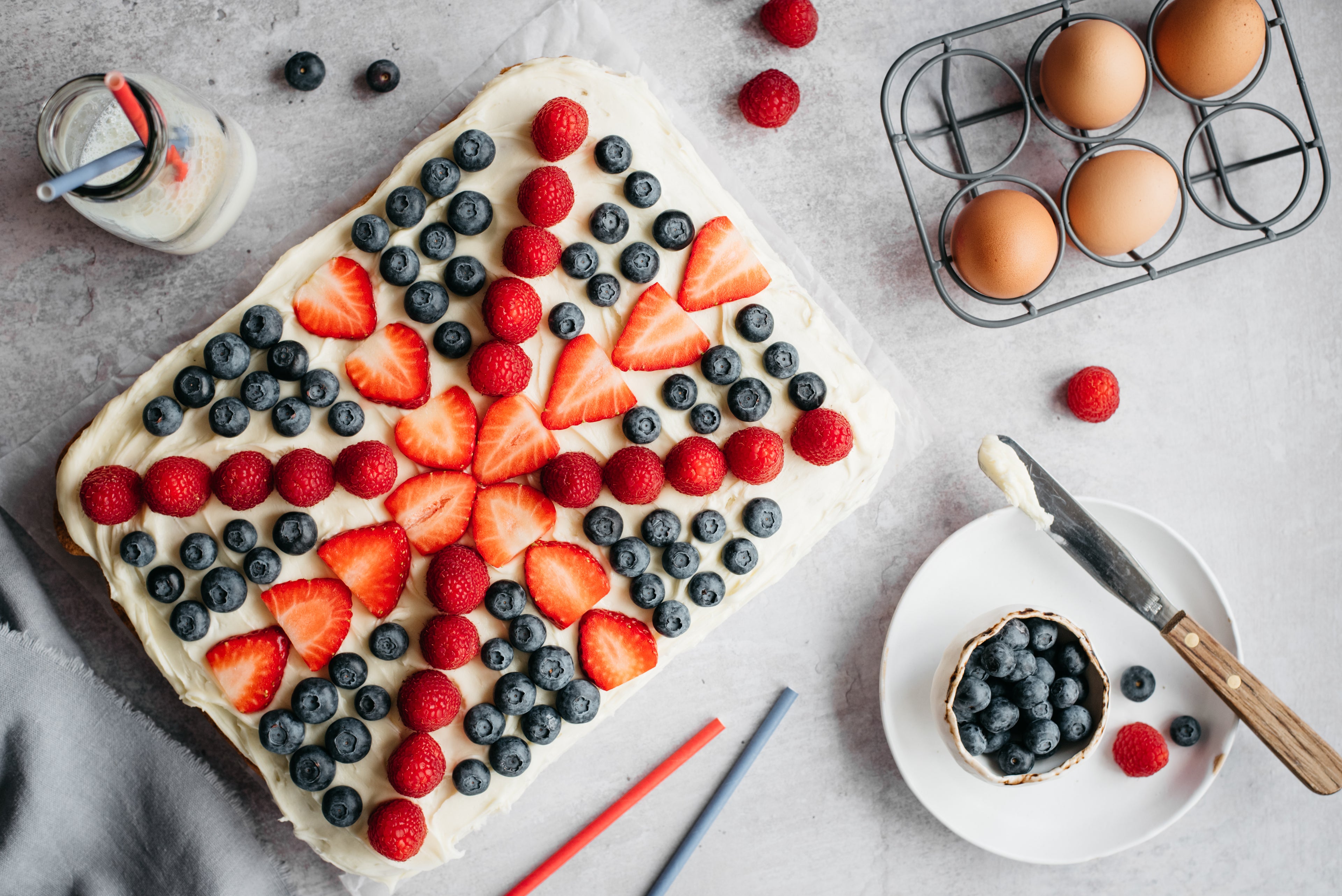 Top view of Union Jack Traybake decorated with seasonal fresh berries for the Jubilee, next to a bowl of blueberries and fresh eggs