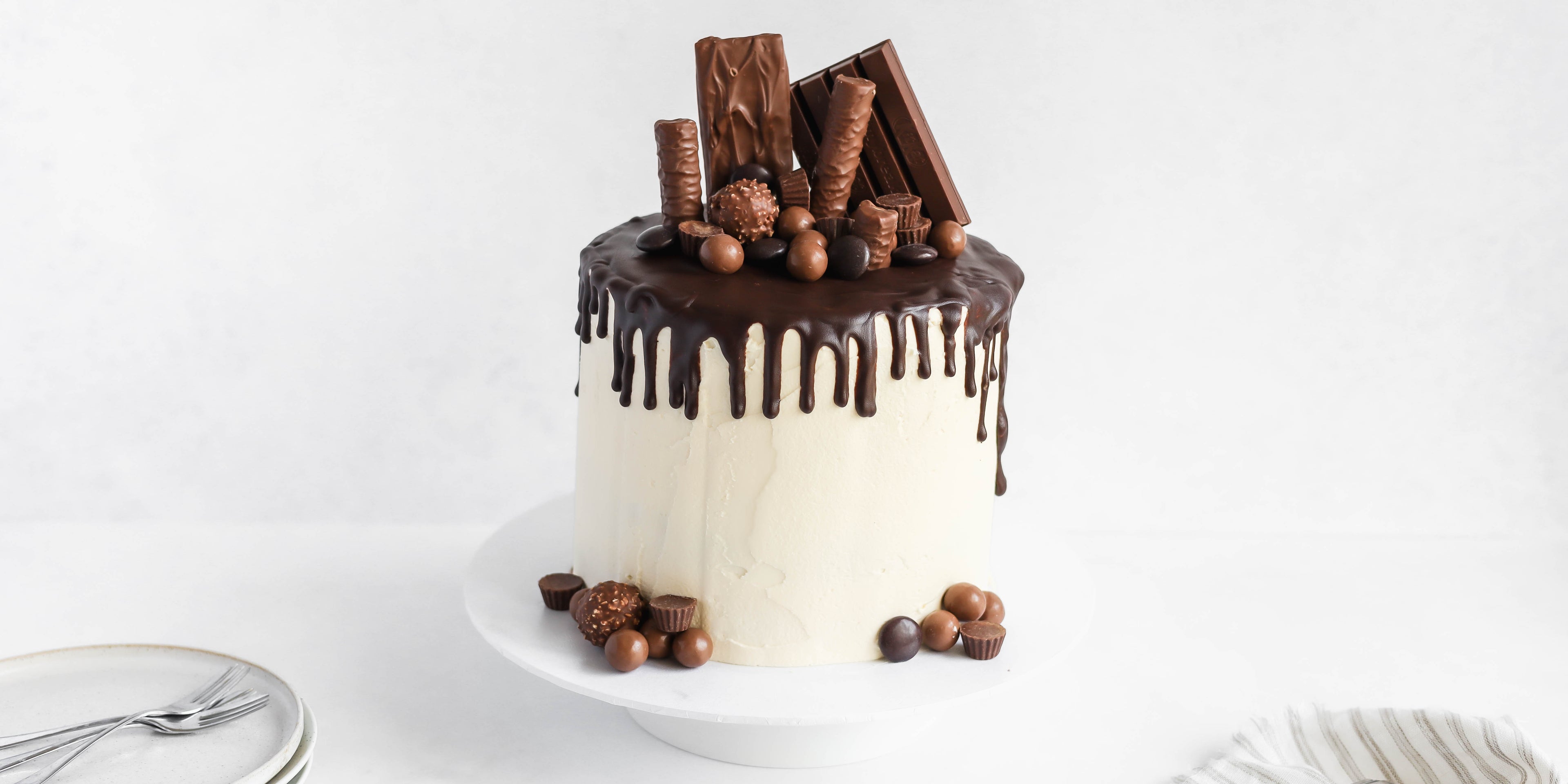 Front view of a Ultimate Birthday Drip Cake topped with chocolate goodie and chocolate drip on vanilla buttercream