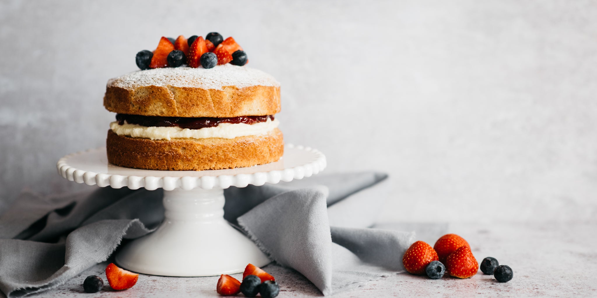 Wholemeal Victoria Sponge on a cake stand, decorated with fresh summer berries.