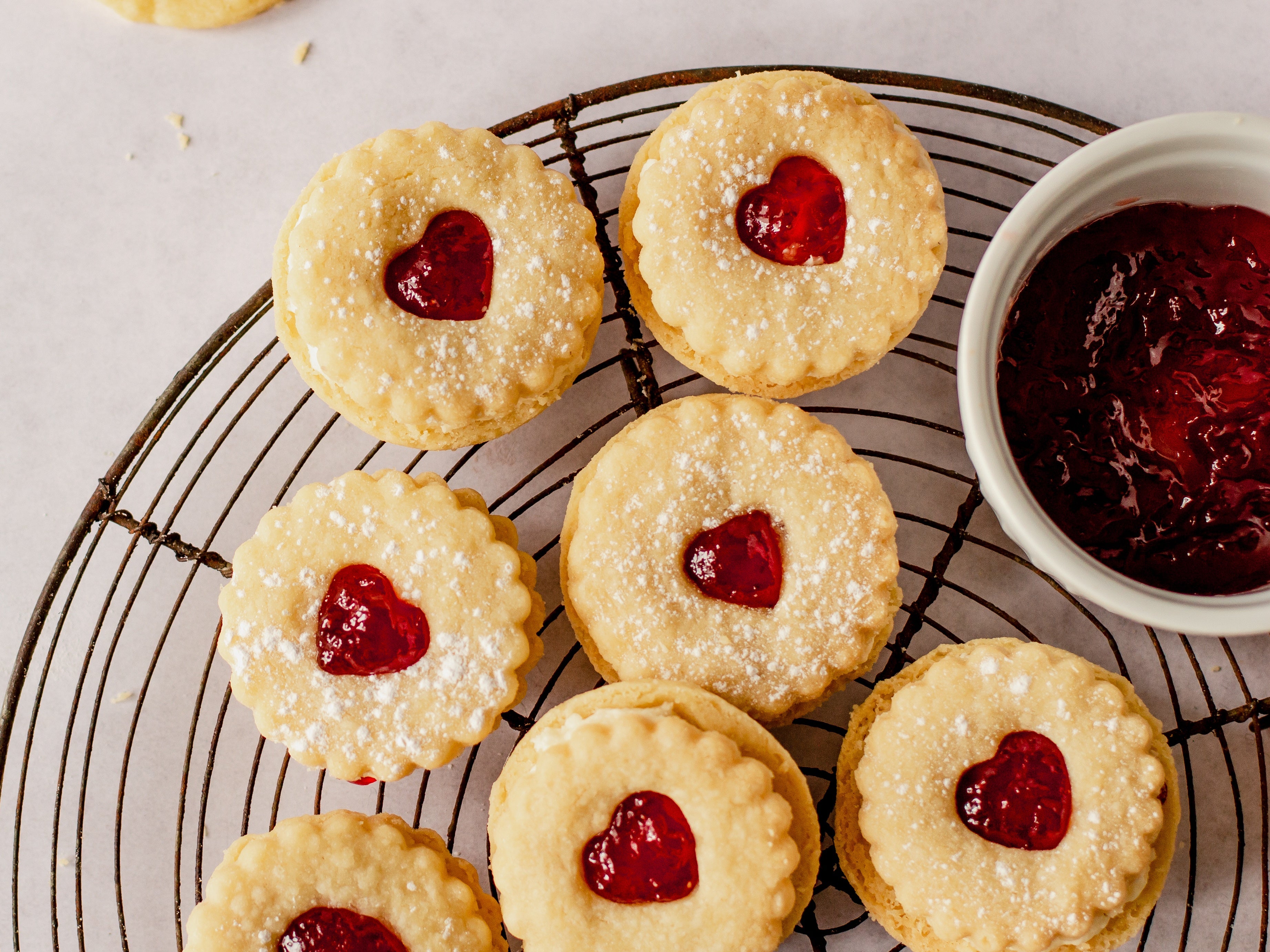 Close up of jammy dodgers on a wire cooling rack with bowl of jam