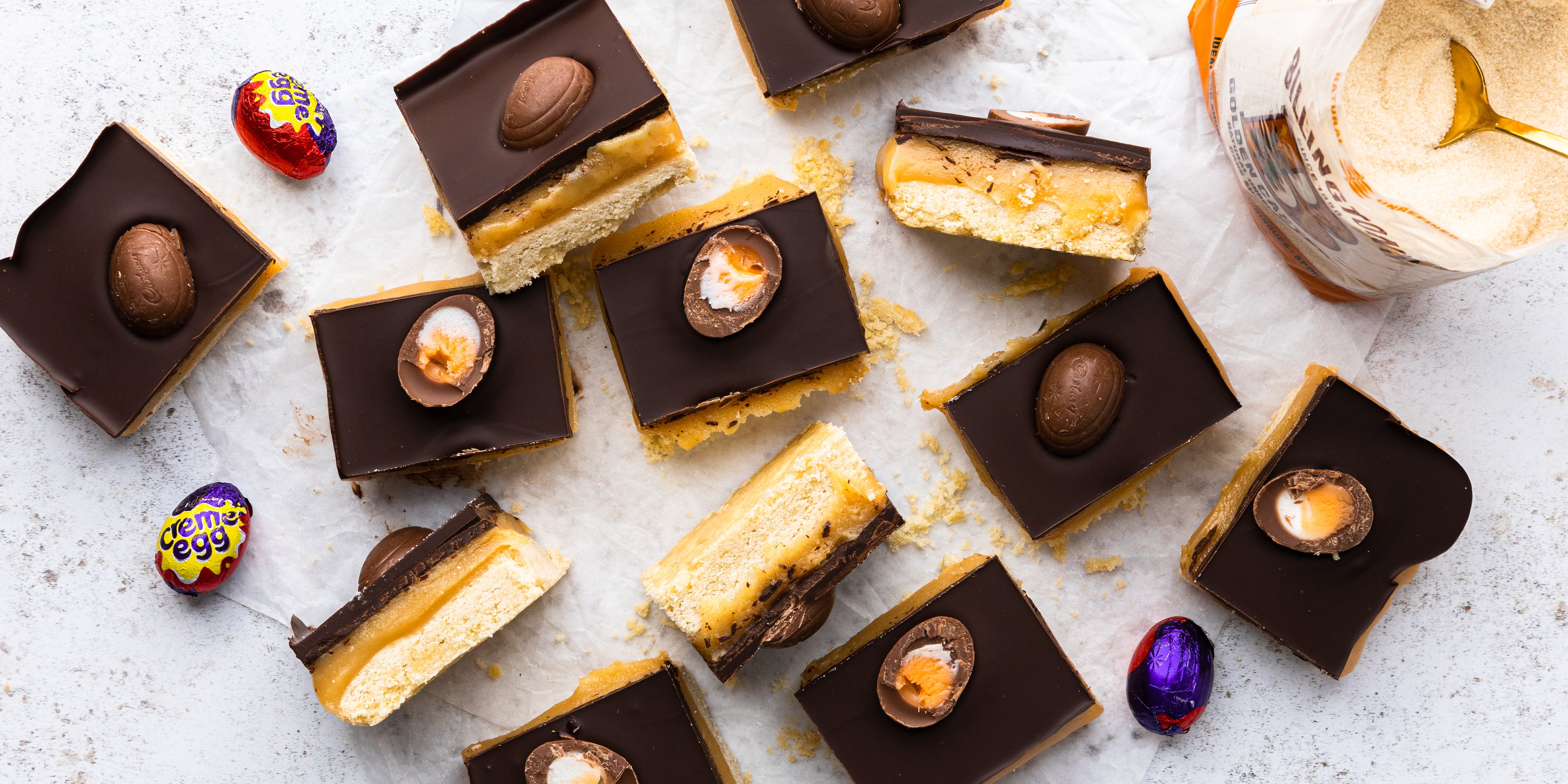 Top down shot of squares of millionaires shortbread with creme eggs and a pack of sugar