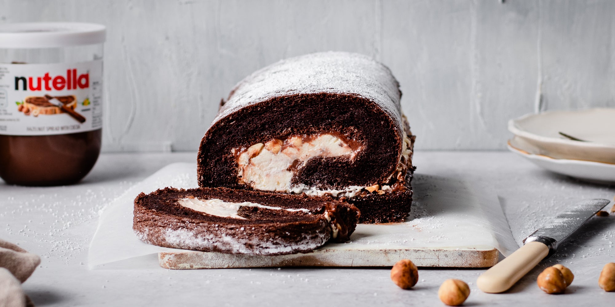 Close up of Chocolate Roulade with a slice cut off showing the thick creamy insides. Jar of Nutella in the background
