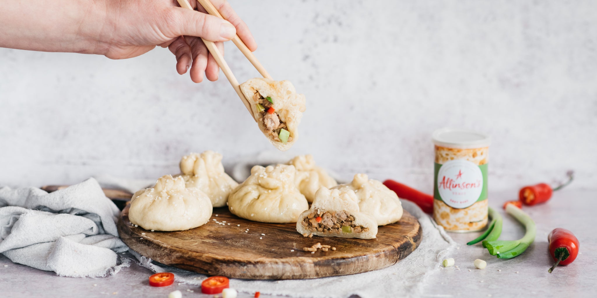 Bao buns on a wooden board, hand reaching in with chopsticks to lift one