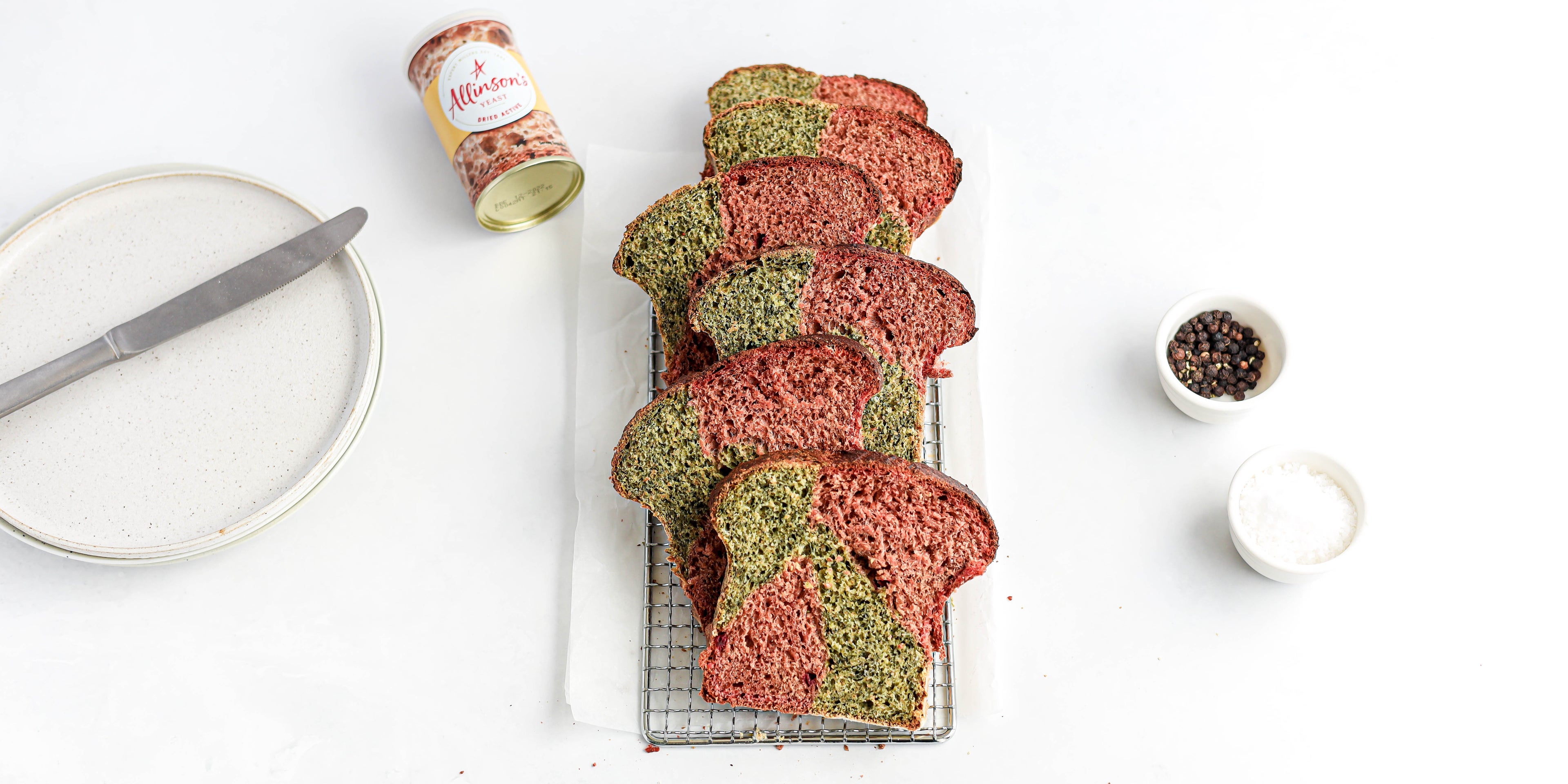 Slices of Marble Vegetable Bread spread out on a wire rack showing the pink and green insides, next to a tin of Allinson's yeast