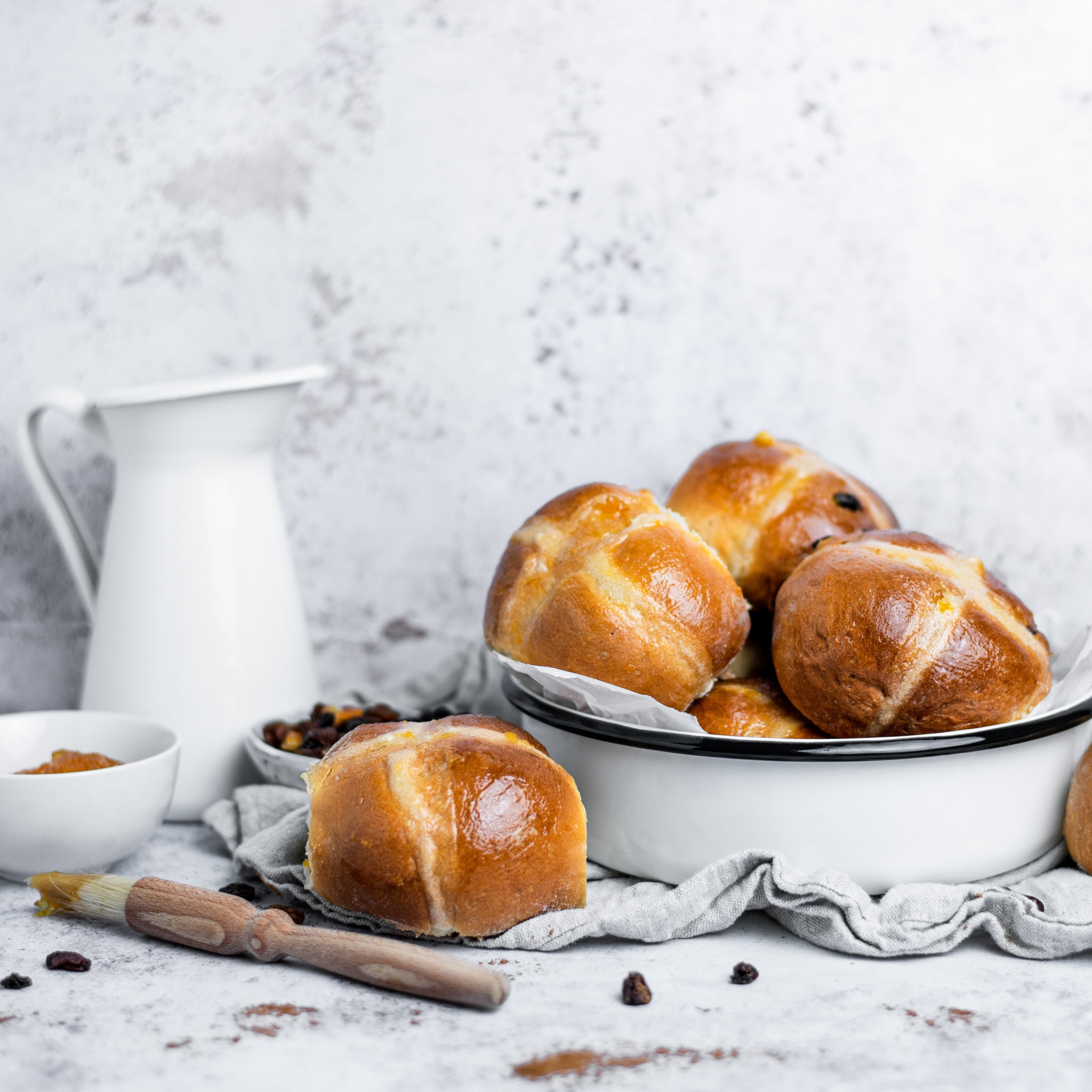 White dish filled with hot cross buns next to a single hot cross bun