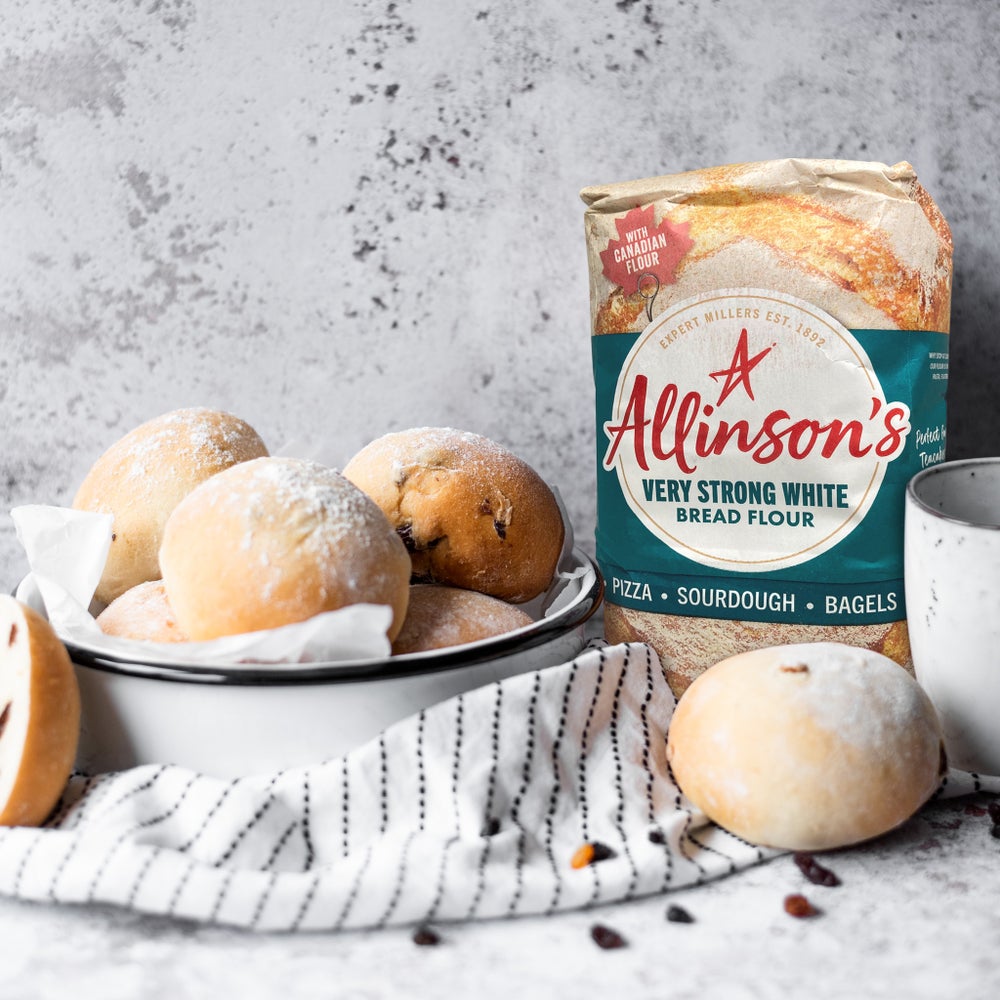 A white dish filled with tea cakes next to a pack of Allinson's very strong white bread flour in front of a grey marble background.