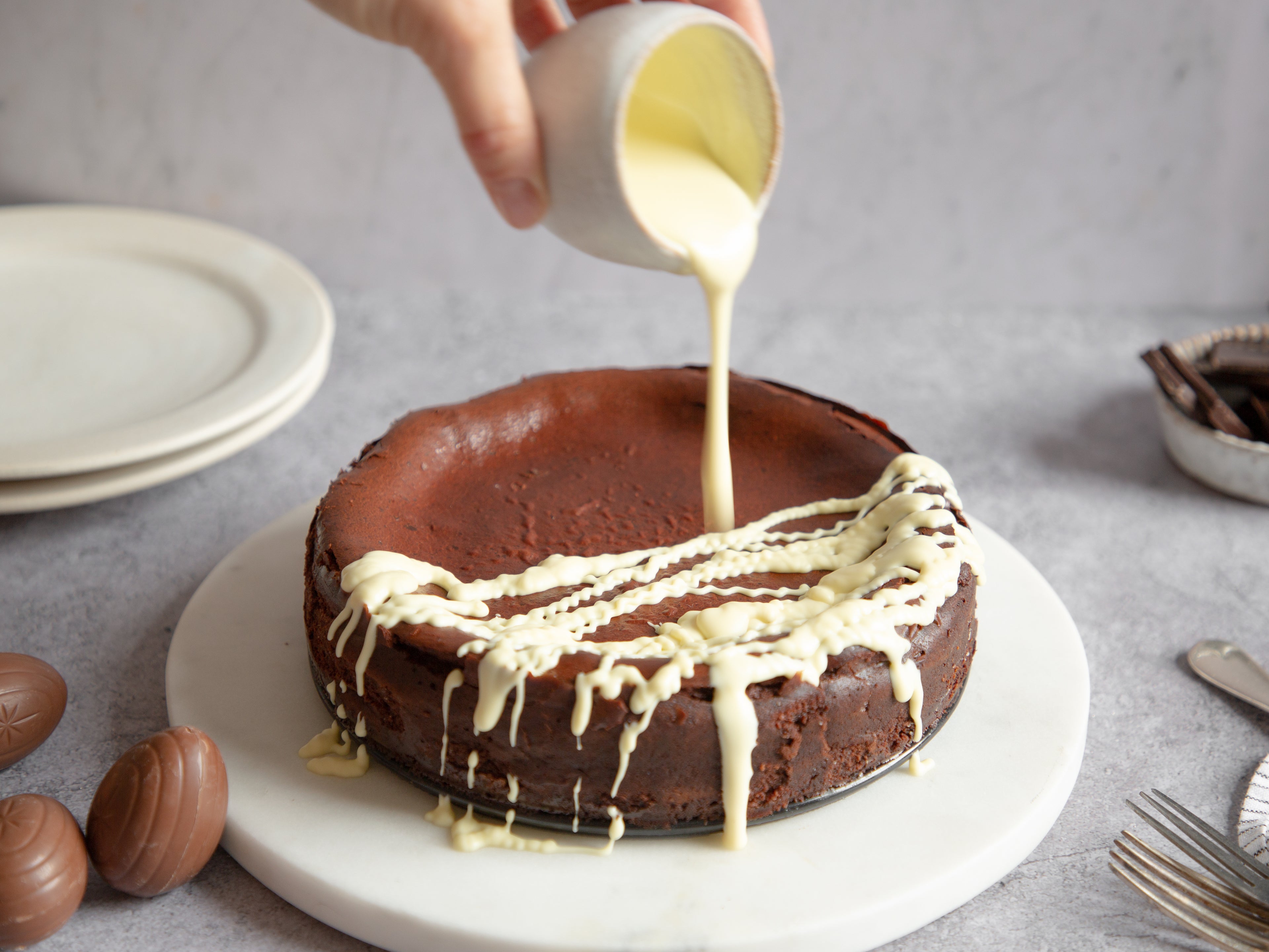 Close up of Chocolate Cheesecake being drizzled with white chocolate 