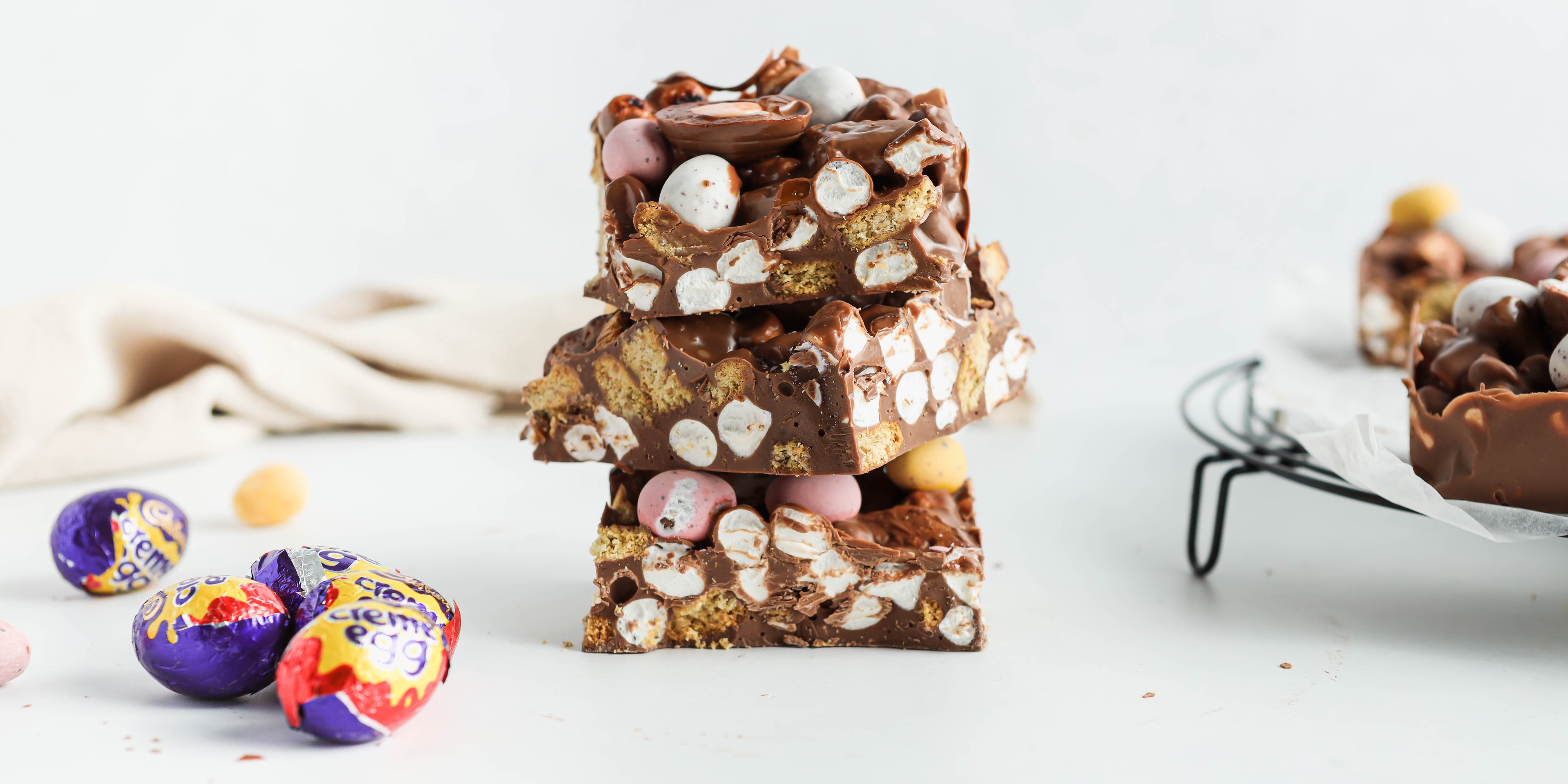 Easter egg rocky road stacked up in 3 pieces with Cadbury Creme Eggs to the side.