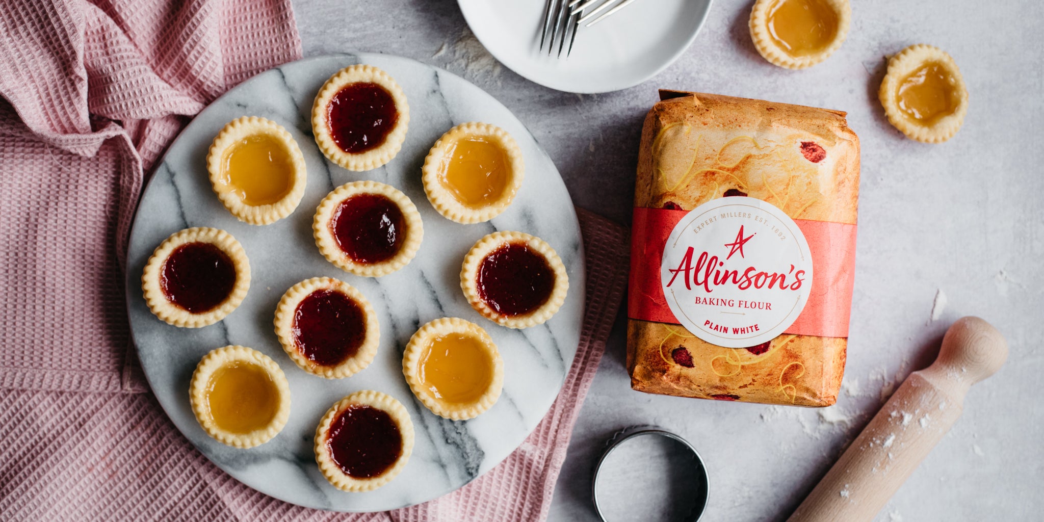 Top view of Strawberry & Apricot Jam Tarts next to a flat lay bag of Allinson's Plain Flour