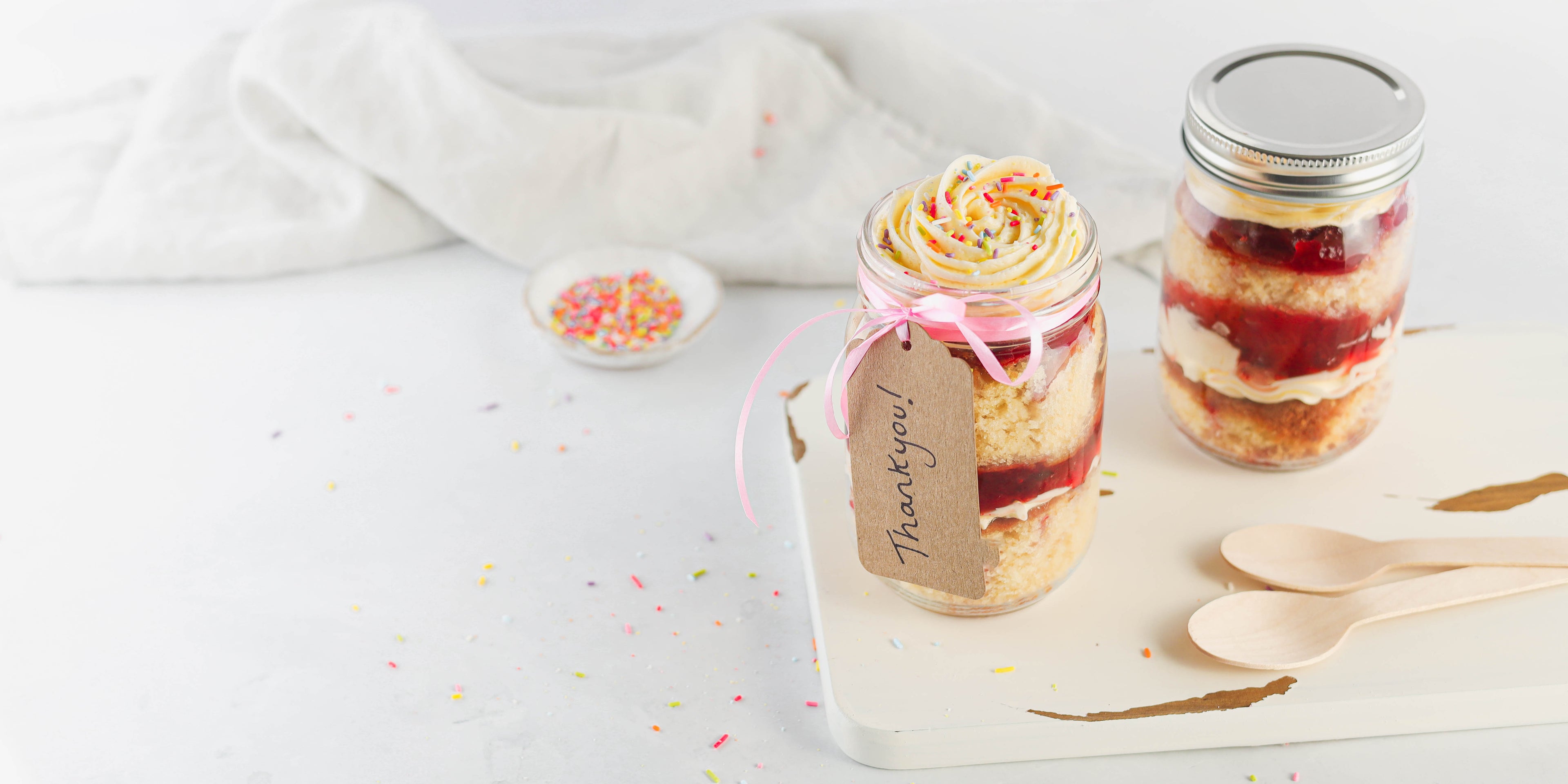 Vanilla Cupcakes in a Jar with a handwritten thank you tag, next to a bowl of sprinkles