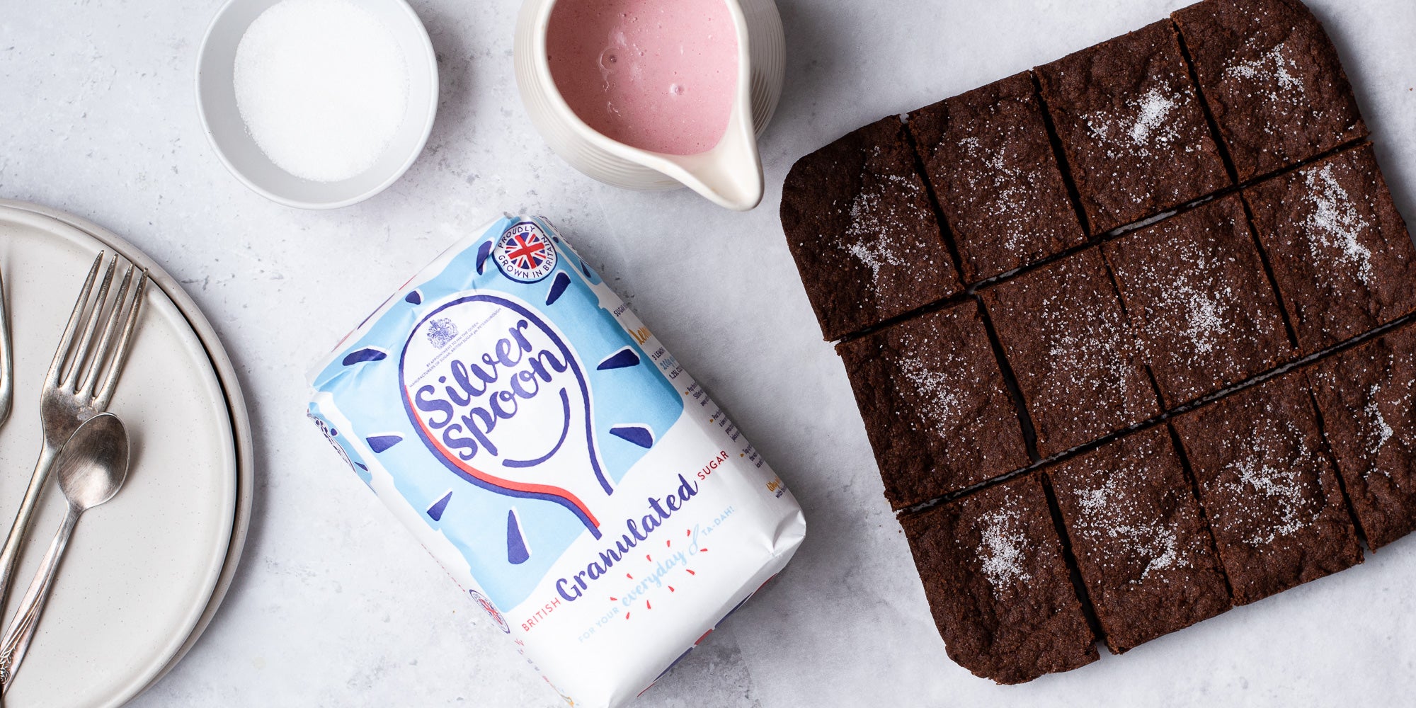 Chocolate Concrete Cake with jug of pink custard and a bag of silver spoon granulated sugar flatlay