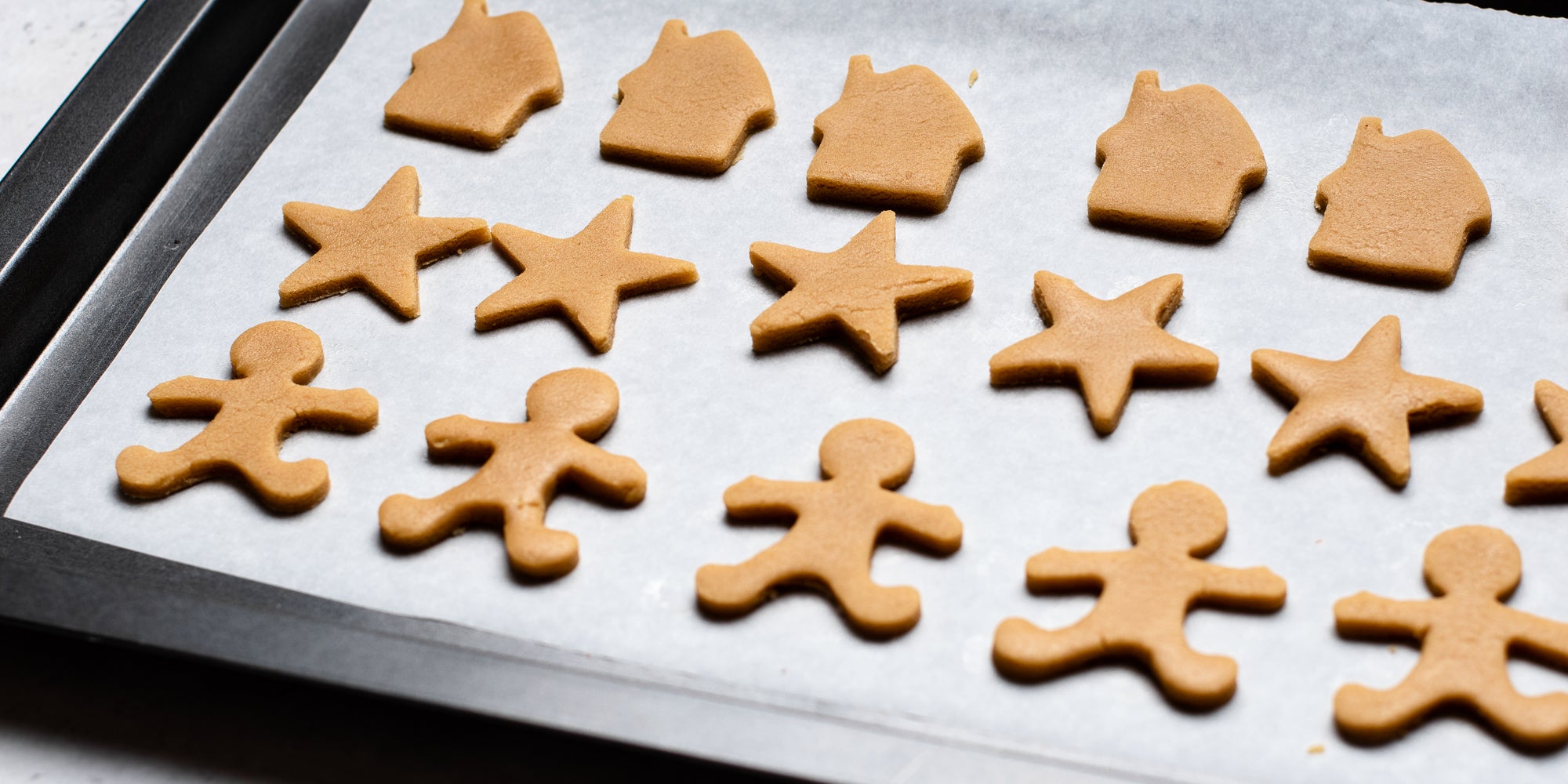 Shapes cut from Gingerbread Dough including, gingerbread men, stars and gingerbread houses lay on baking paper on a baking tray