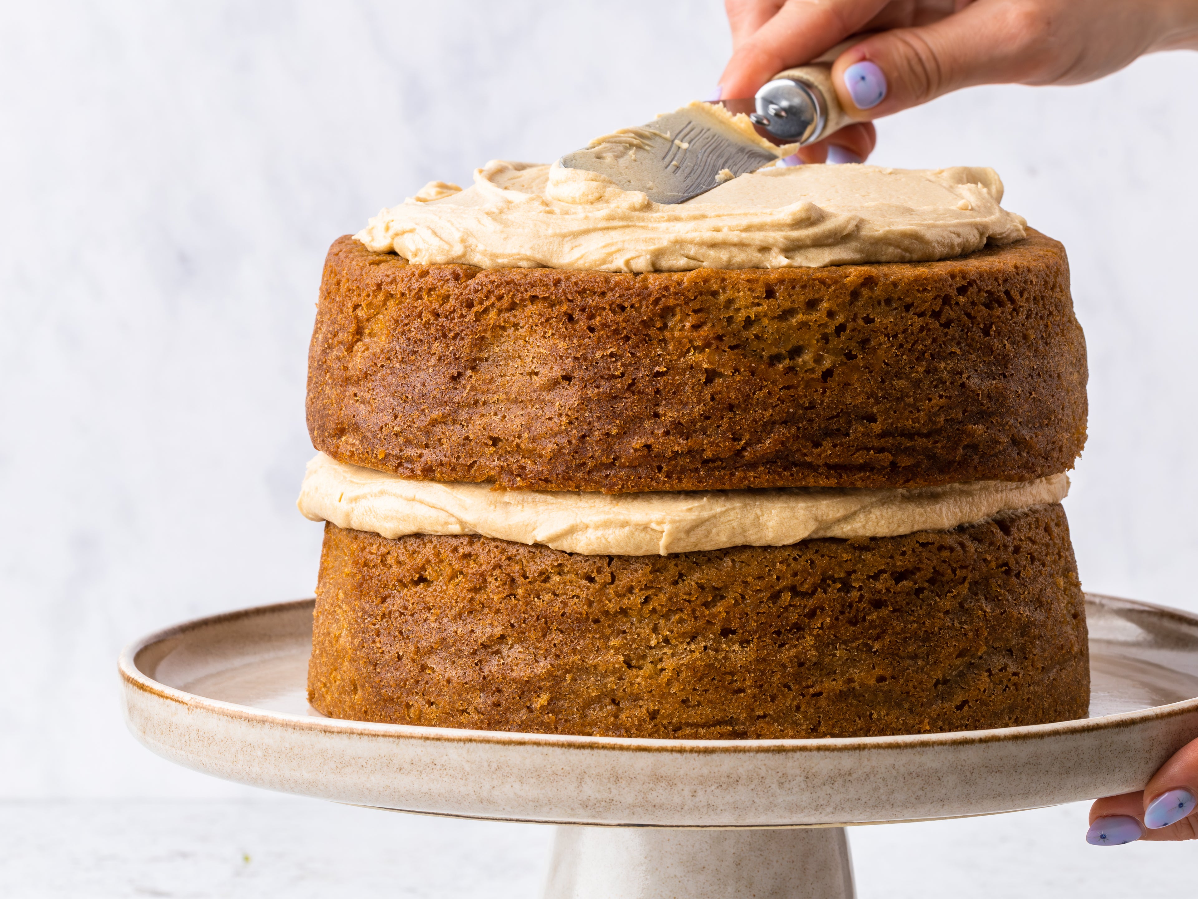 Coffee cake sponge on a cake stand with coffee buttercream being spread on top of it
