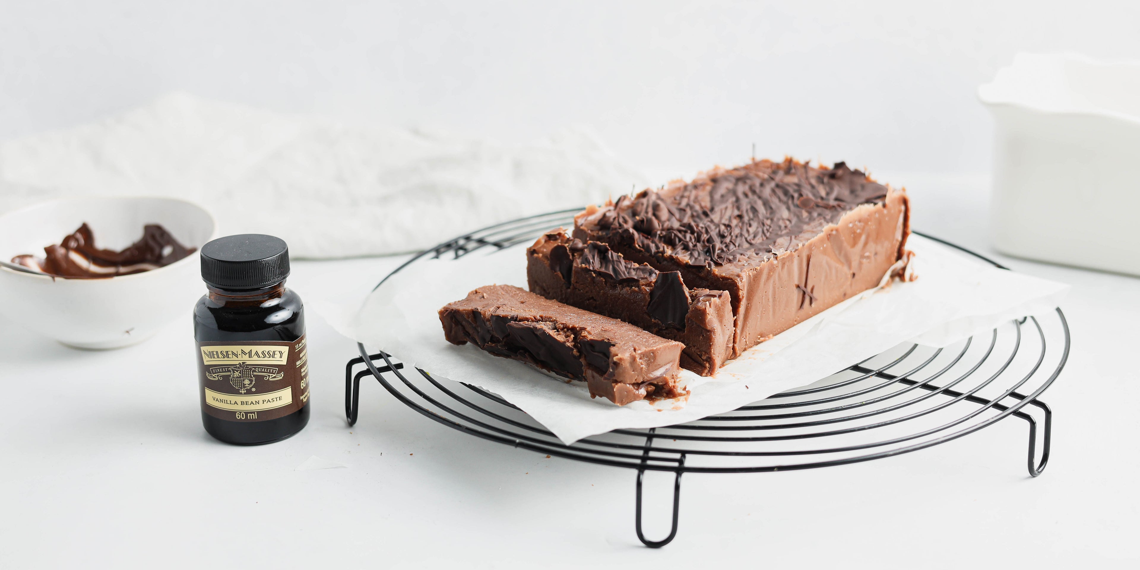 Side on view of chocolate halva slices on a plate next to a bottle of nielsen massey vanilla extract