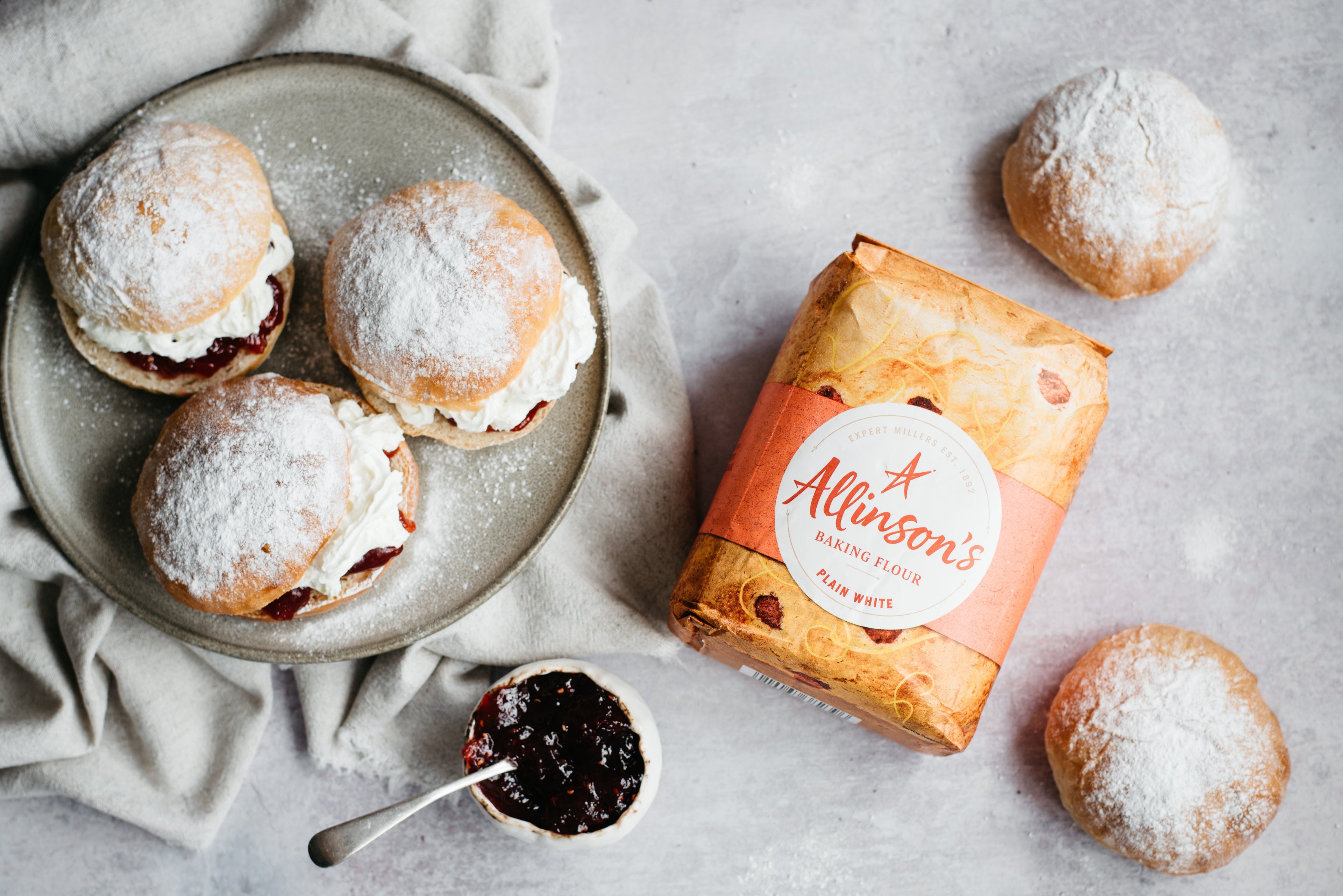 Flat lay of Devonshire Splits next to a bag of Allinson's plain flour and a bowl of jam.