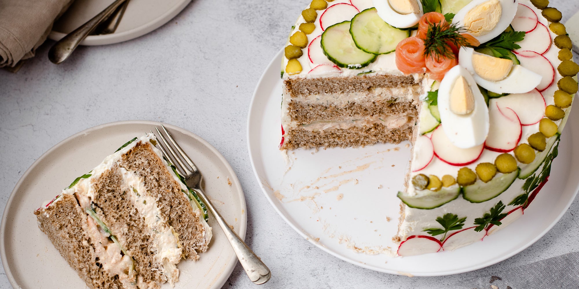 Smörgåstårta Sandwich Cake on a white plate with a slice cut out of it