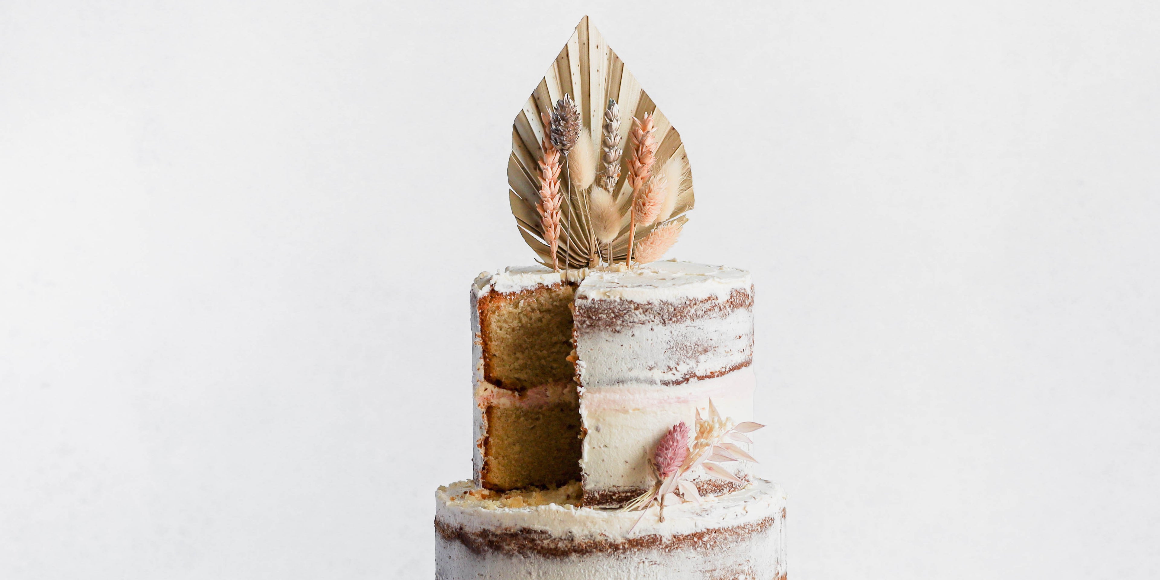 A close up view of a three tiered naked vanilla celebration cake with a slice cut out