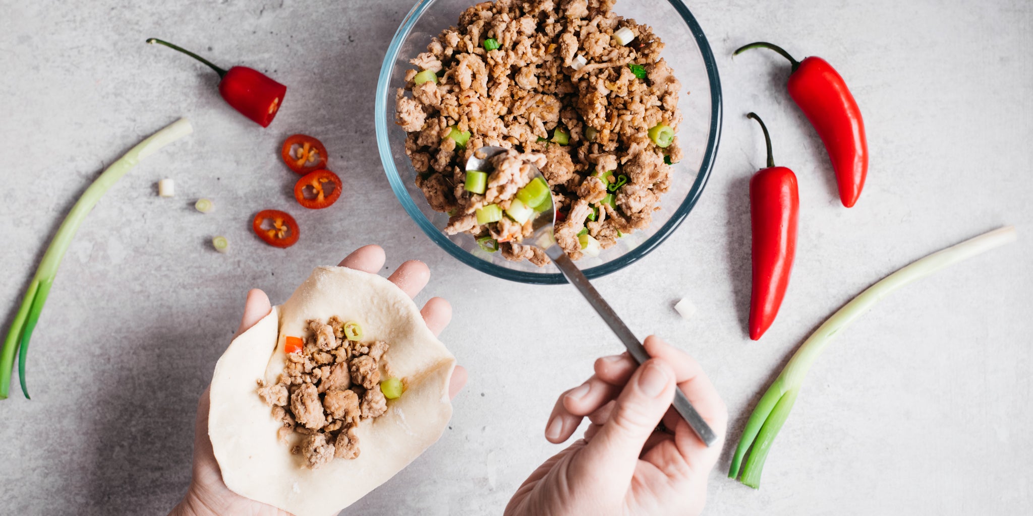 Hand spooning meat filling into a bao bun