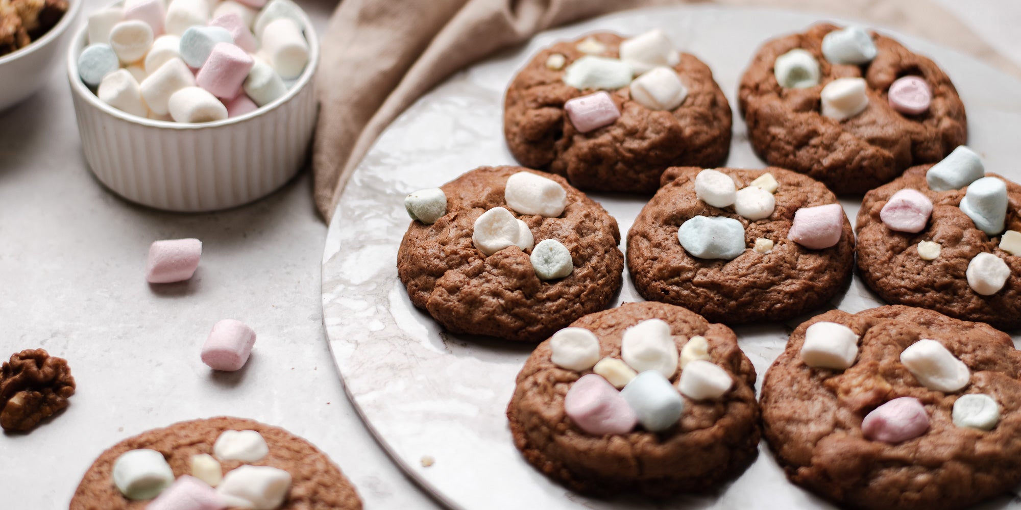 A batch of Rocky Road Cookies topped with marshmallows next to a ramekin of mini marshmallows 