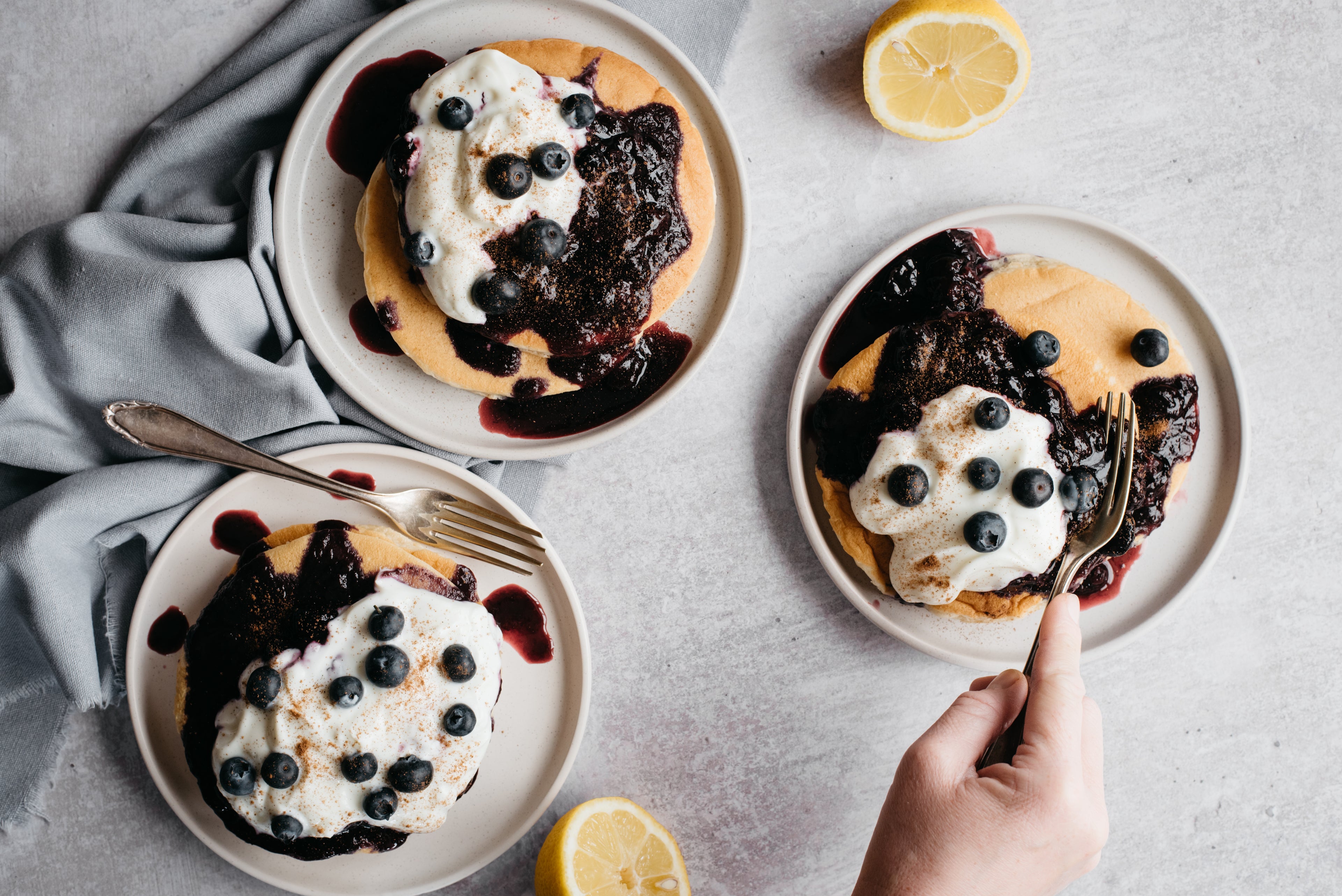 Cinnamon Pancakes with Blueberry Compote served on plates and with a dollop of yoghurt, with a fork scooping into a stack