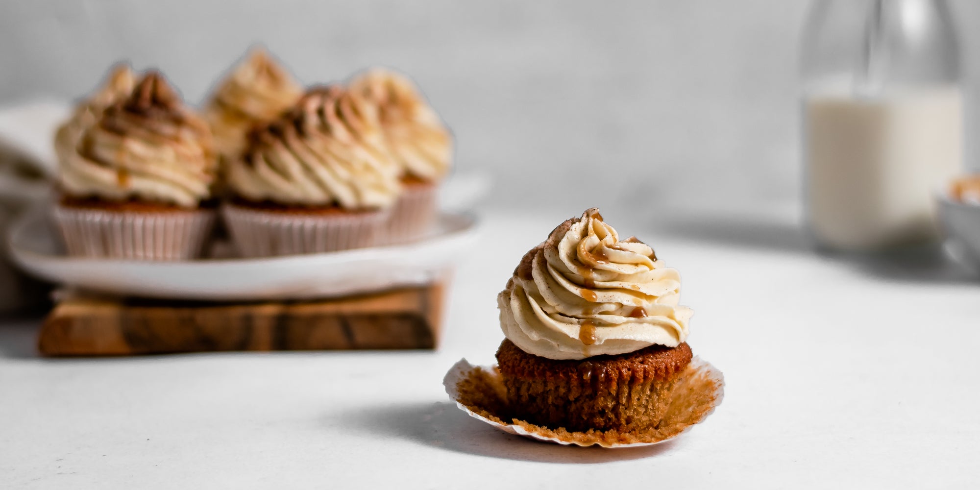 Gingerbread Cinnamon Cupcake with caramel sauce dripping down the buttercream, batch of Gingerbread Cinnamon Cupcakes in the background